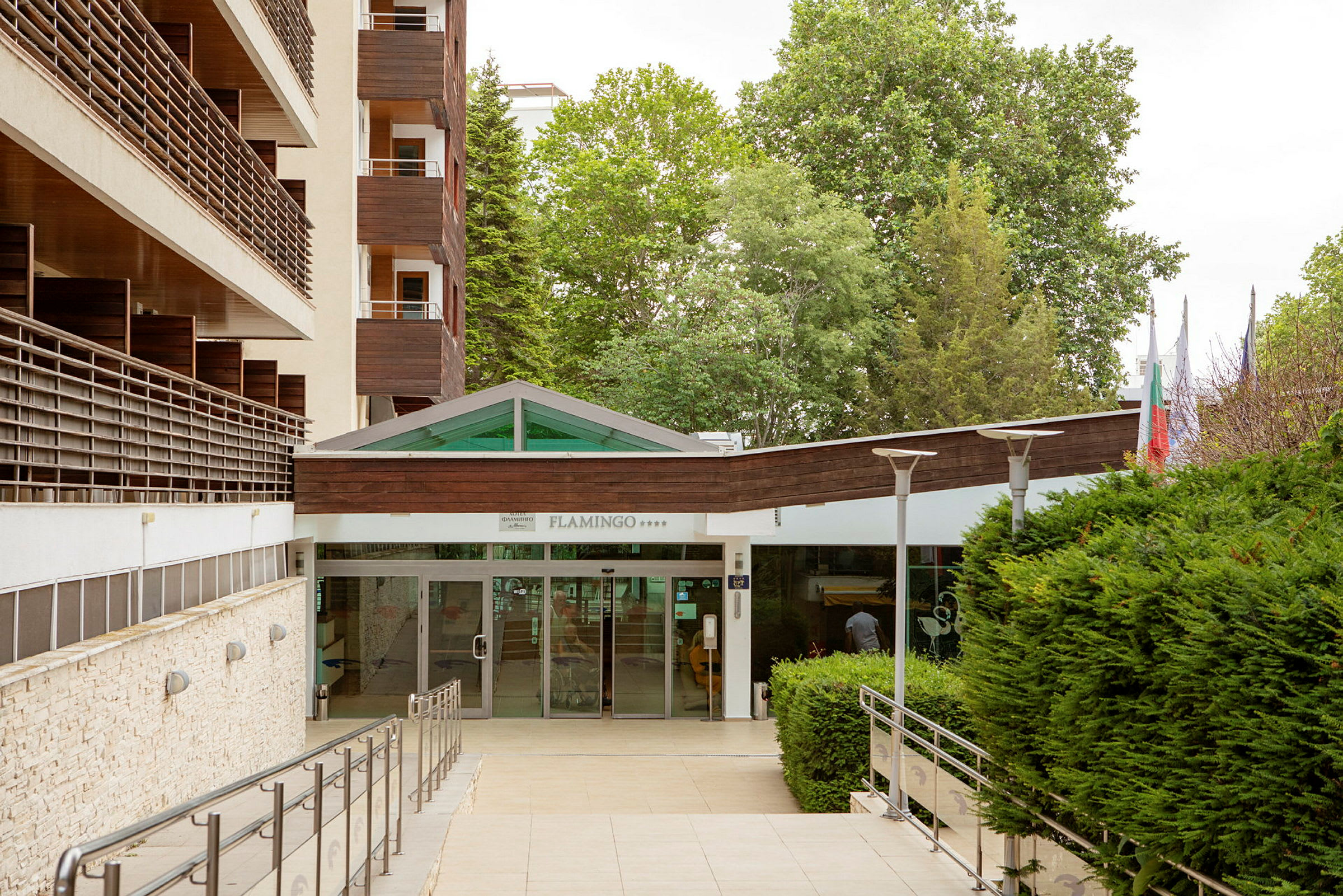 Hotelindgang med glasdøre og omkringliggende grønt område. (AI-genereret tekst)