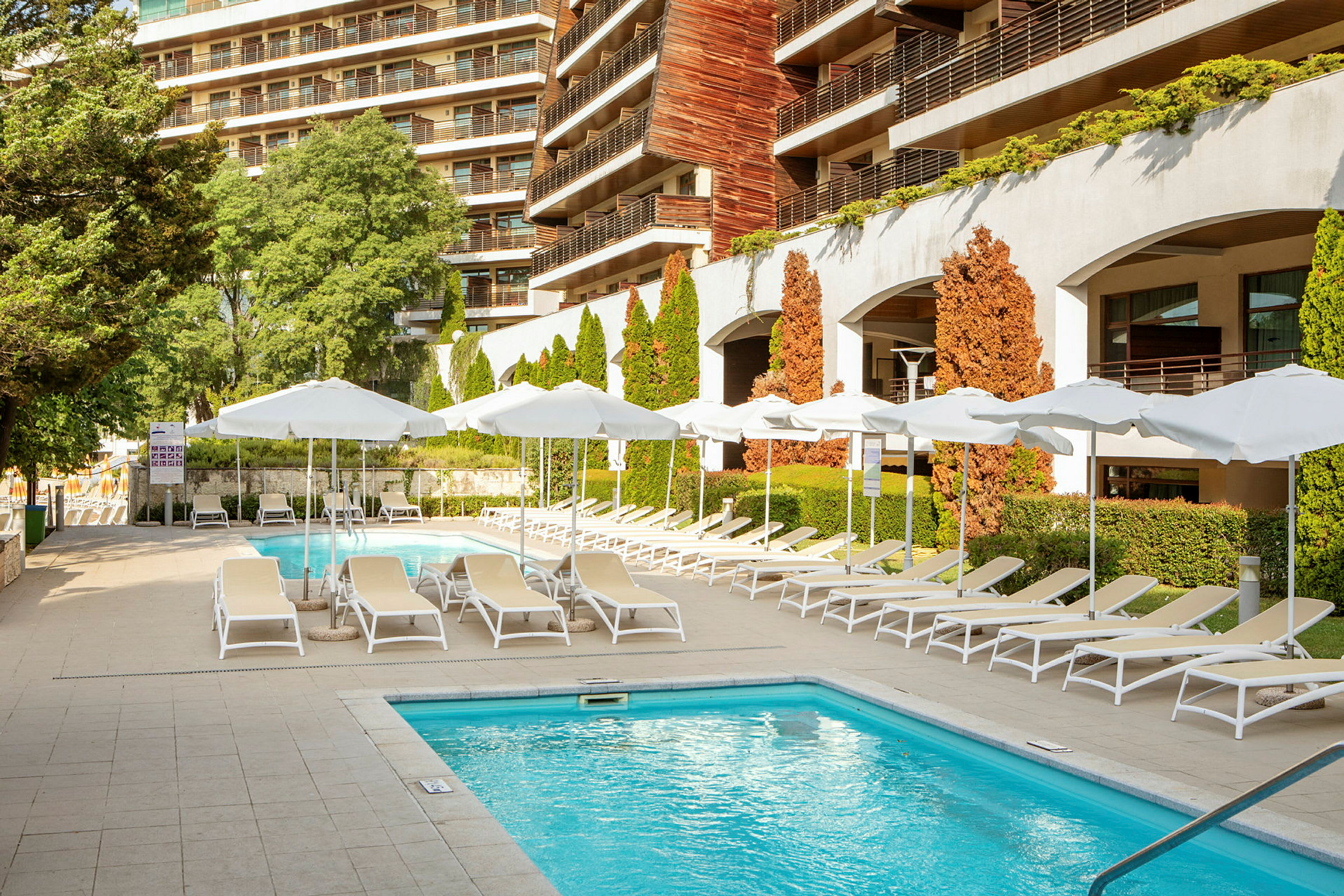 Udendørs pool med liggestole og parasoller ved et hotel. (AI-genereret tekst)