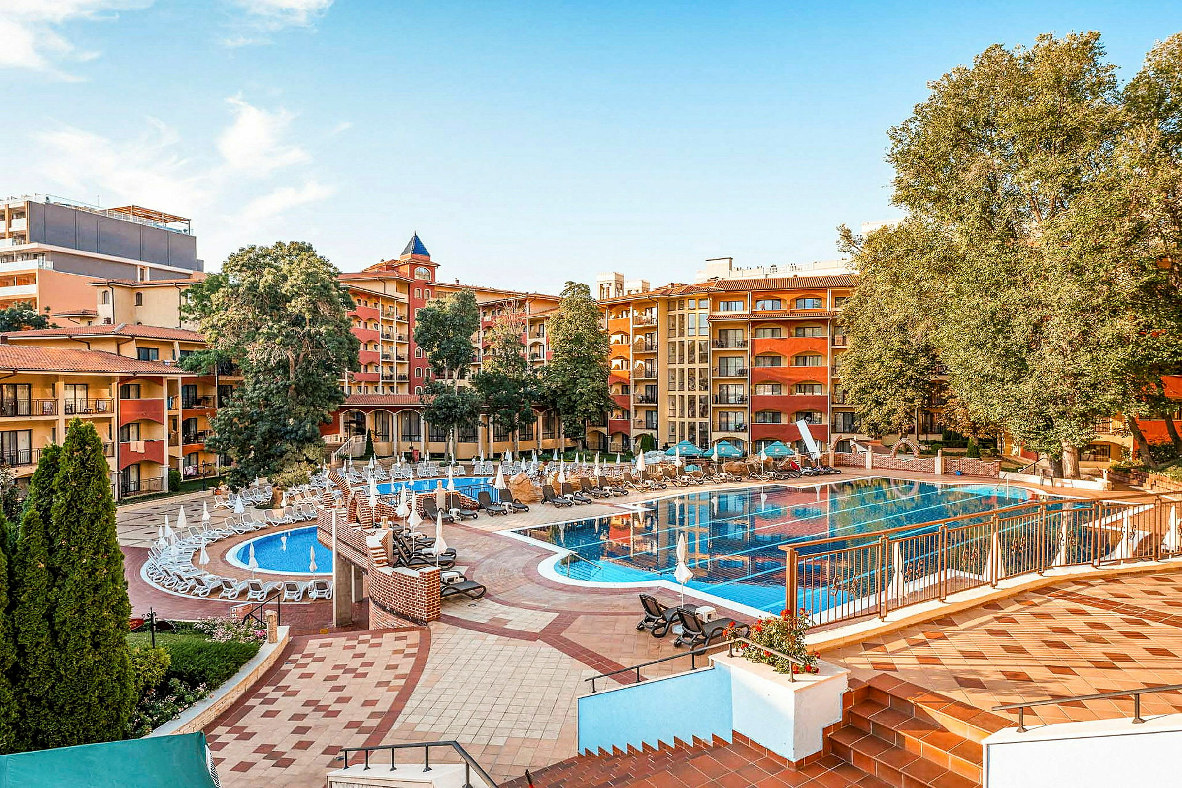 Hotellets poolområde med liggestole, parasoller og bygninger i baggrunden. (AI-genereret tekst)