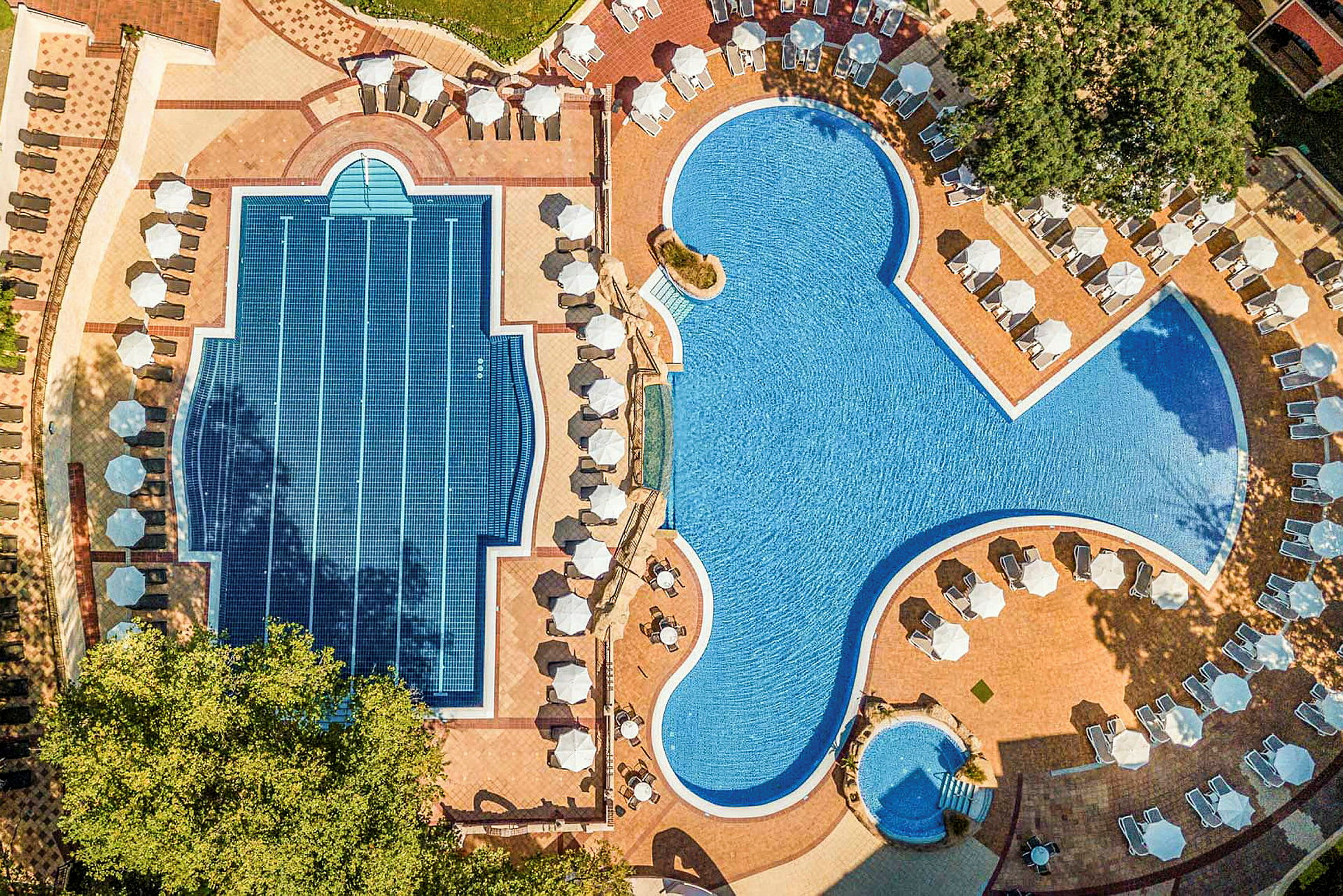 Luftfoto af to forskellige pools med liggestole og parasoller omkring. (AI-genereret tekst)
