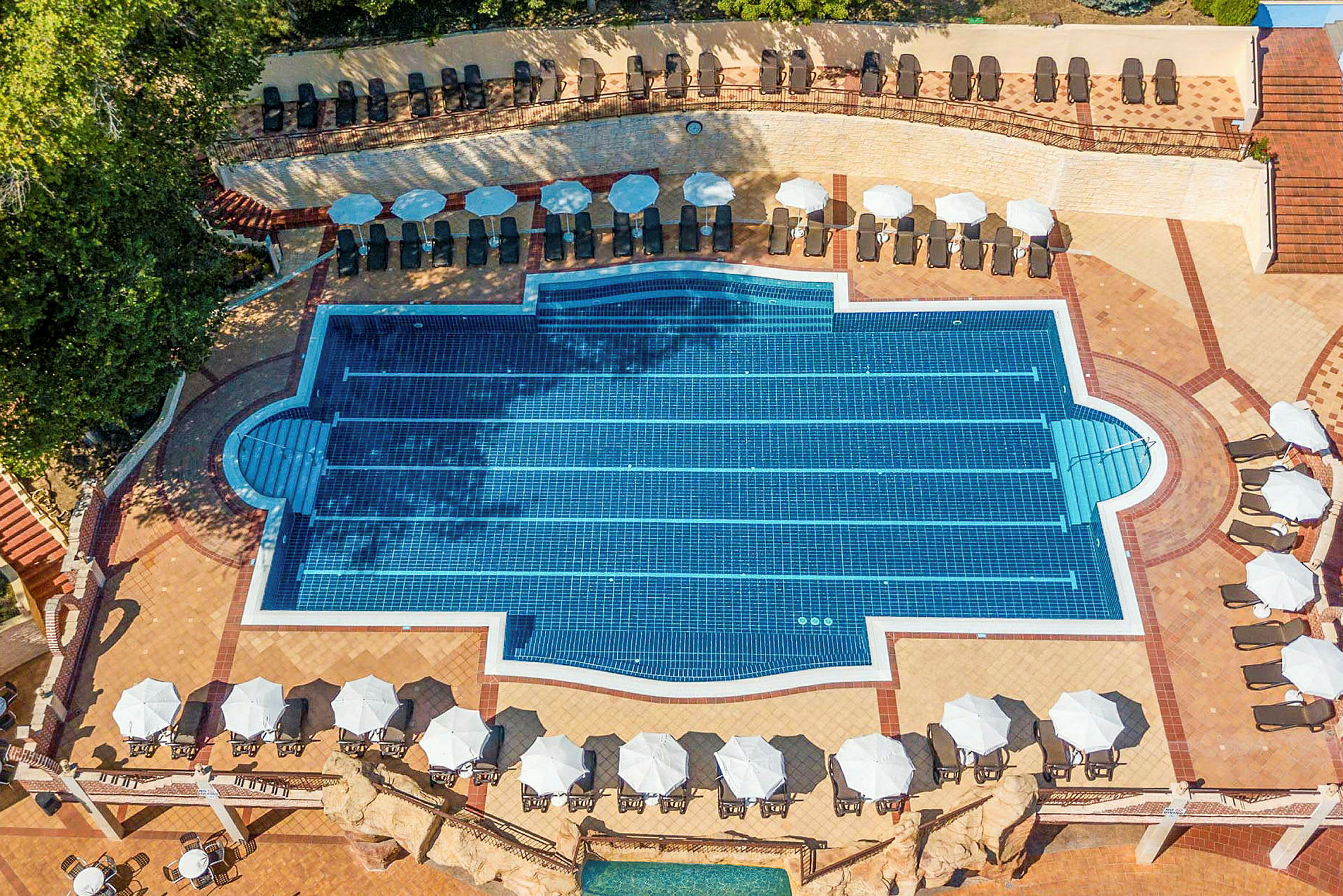 Udendørs swimmingpool med liggestole og parasoller langs kanten. (AI-genereret tekst)