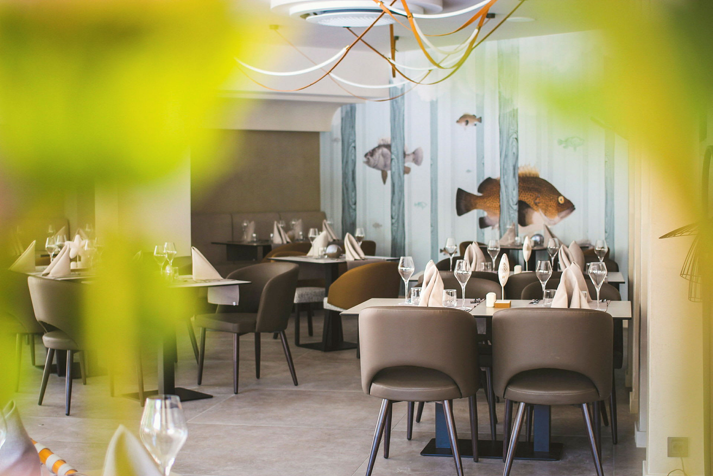 Restaurant med dækkede borde, brune stole og dekorationer med fiskemotiv på væggen. (AI-genereret tekst)