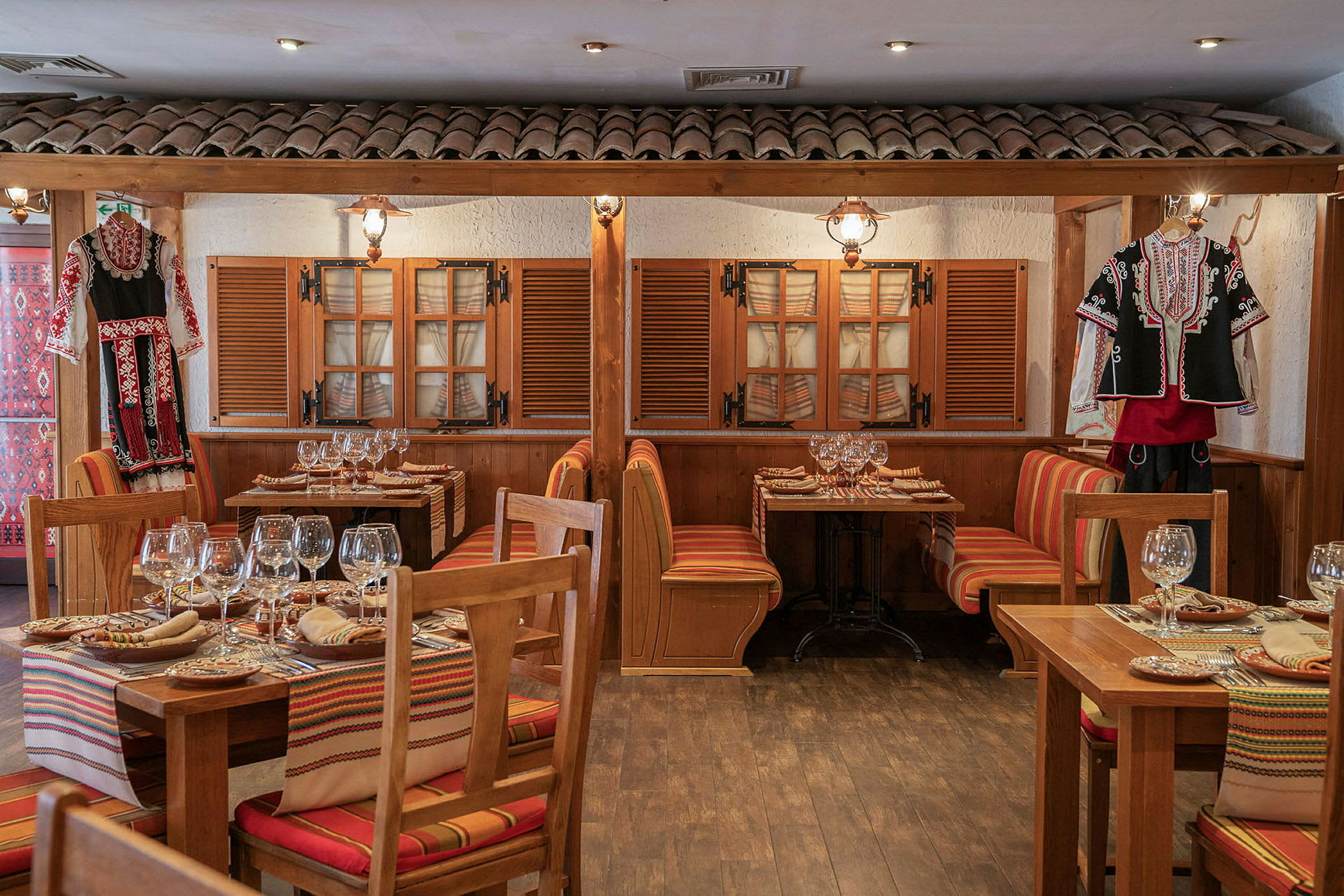 Billede af en restaurant med traditionelle træborde, farverige siddepuder og folkedragter som dekoration. (AI-genereret tekst)