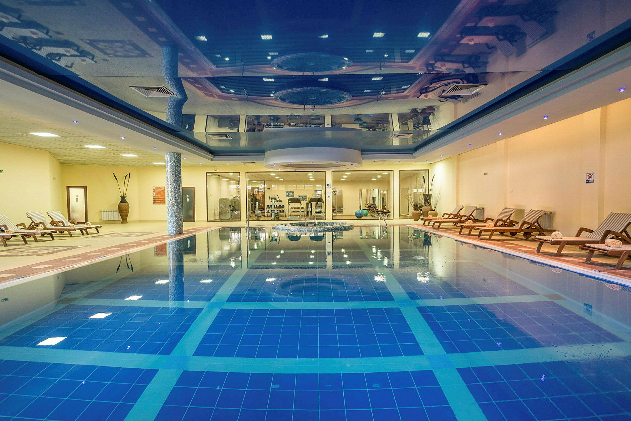 En indendørs pool med liggestole og træningsudstyr i baggrunden. (AI-genereret tekst)