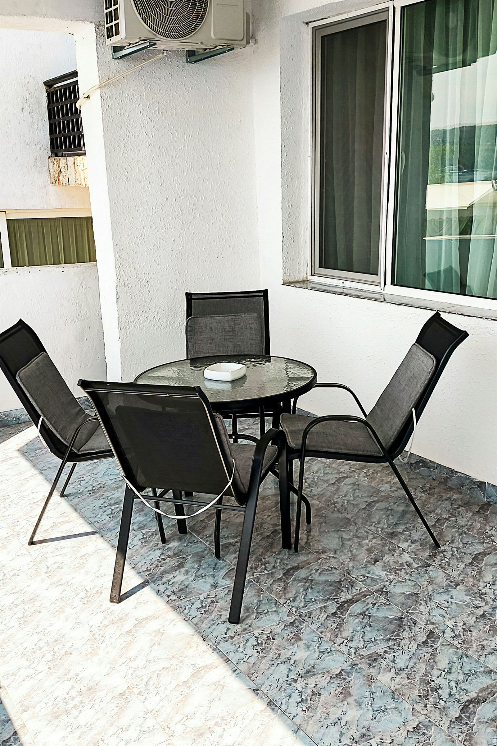 En udendørs terrasse med fire stole omkring et rundt bord med glasplade. (AI-genereret tekst)