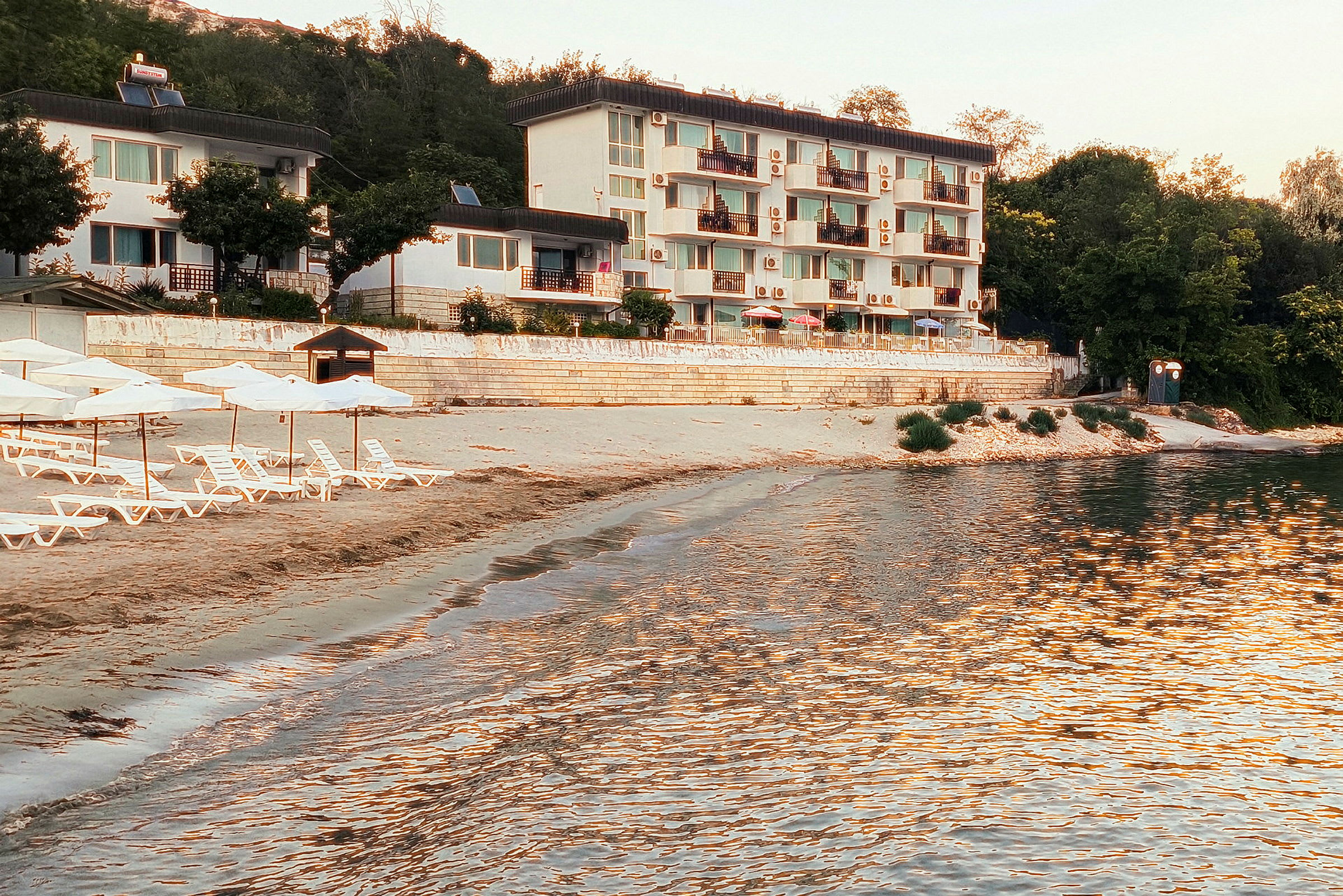 Strand med liggestole og parasoller foran en hvid bygning. (AI-genereret tekst)