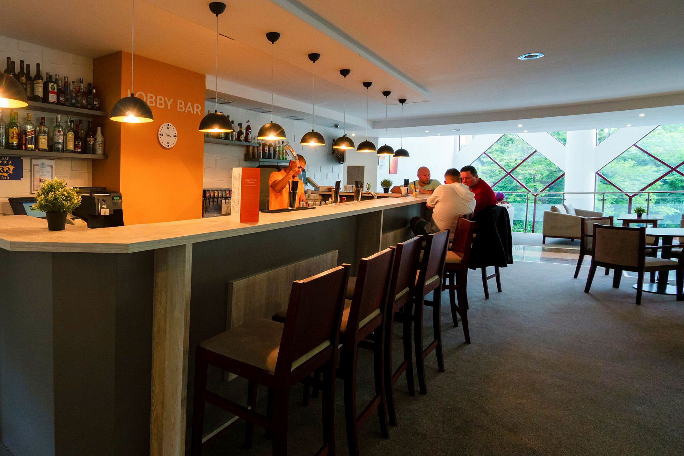 En lobbybar med belysning, stole og mennesker, der sidder ved skranken. (AI-genereret tekst)