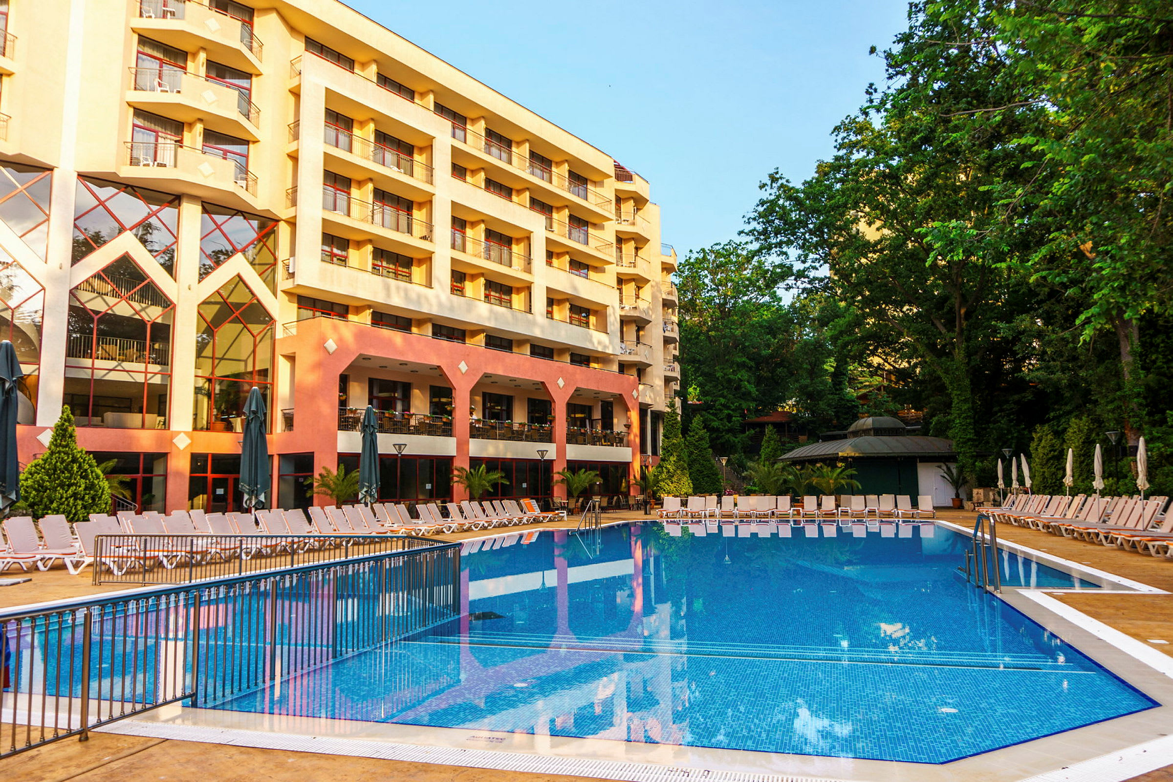 Hotellets facade med en pool og liggestole i forgrunden. (AI-genereret tekst)