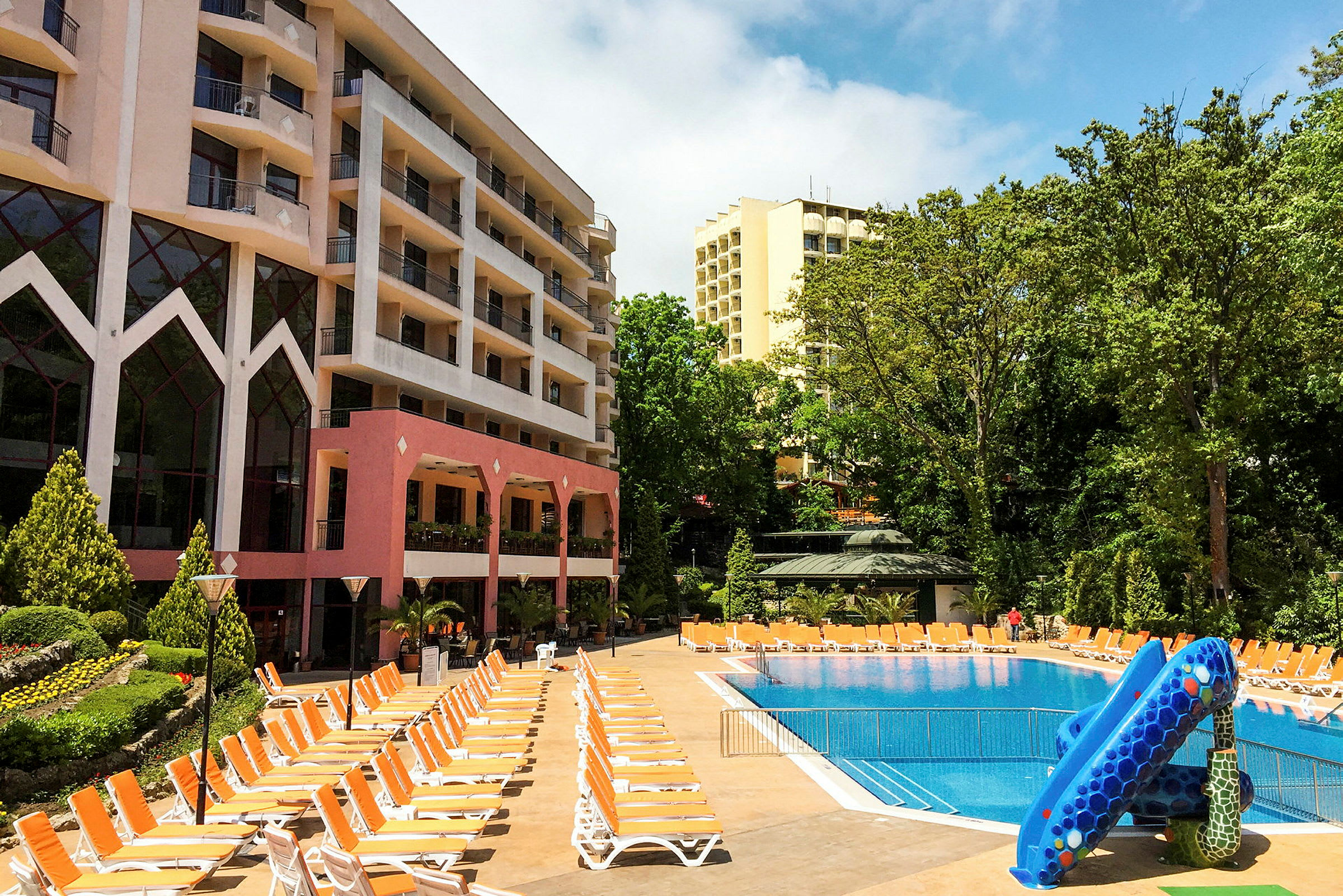 Hotelbygninger ved en udendørs pool med liggestole og vandrutsjebane. (AI-genereret tekst)