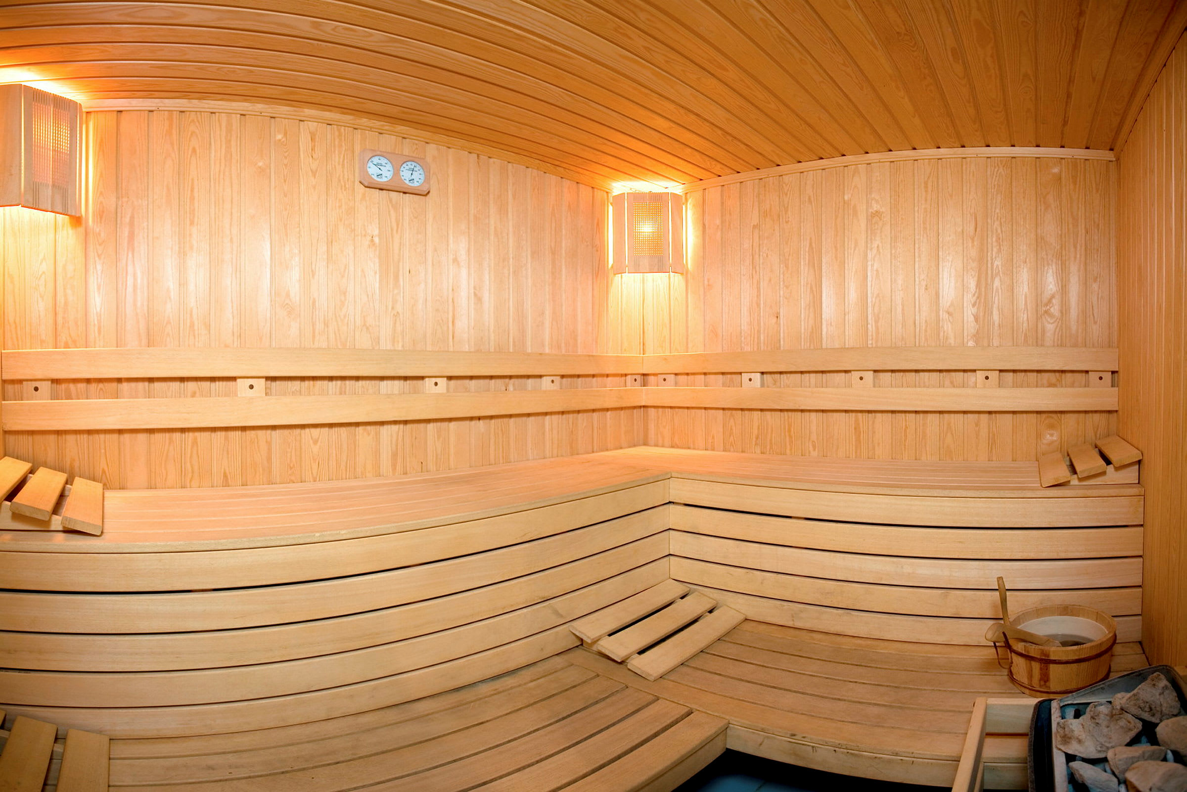 Interiøret af en træbeklædt sauna med bænke og en spand. (AI-genereret tekst)