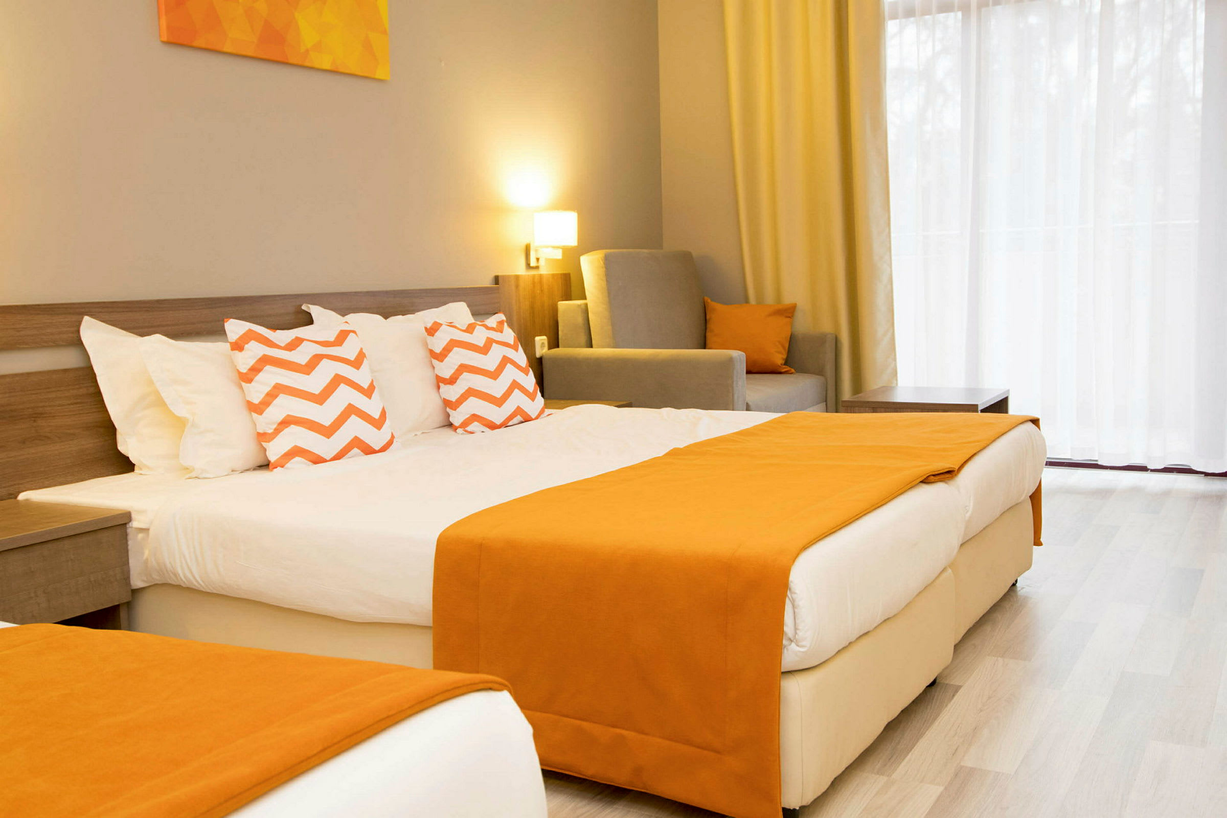 Hotelværelse med en dobbeltseng udsmykket med orange tæpper og puder med zigzag-mønster. (AI-genereret tekst)
