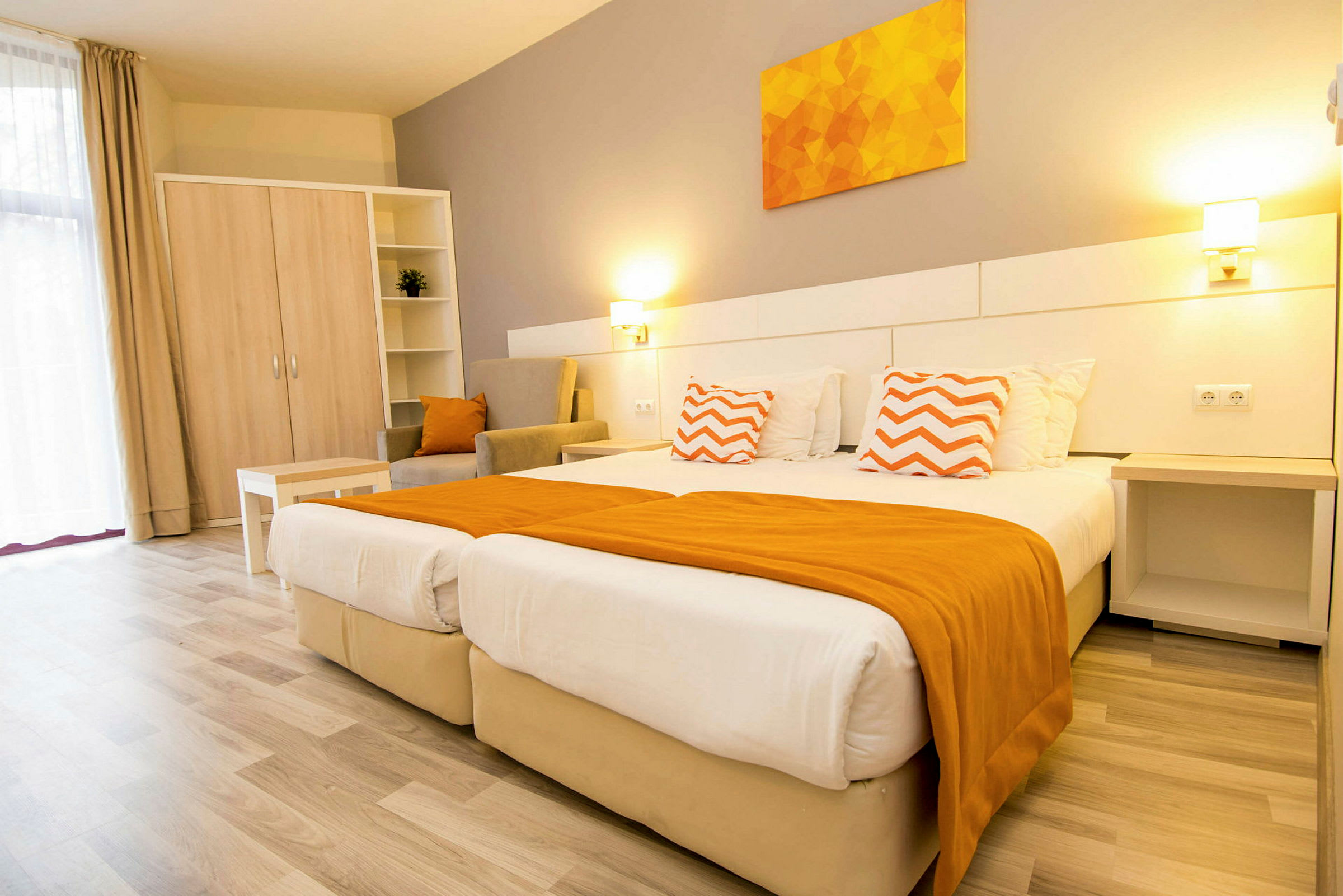 Et lyst hotelværelse med to senge, orange detaljer og møbler. (AI-genereret tekst)