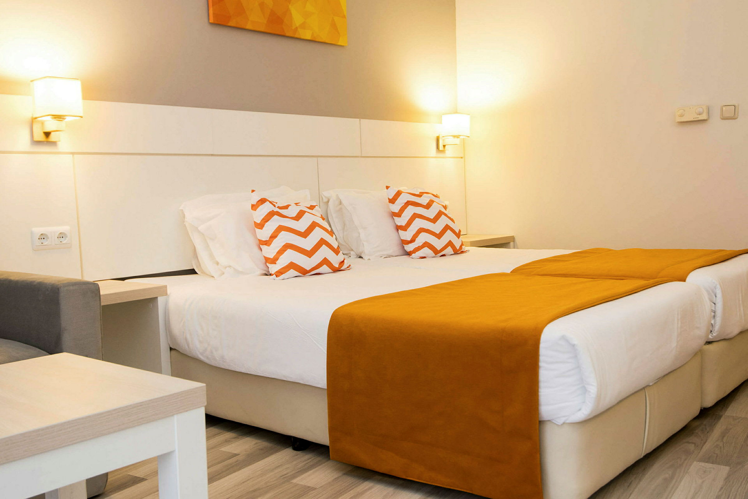 Et hotelværelse med to enkeltsenge med orange sengetæpper og pyntepuder med zigzagmønster. (AI-genereret tekst)