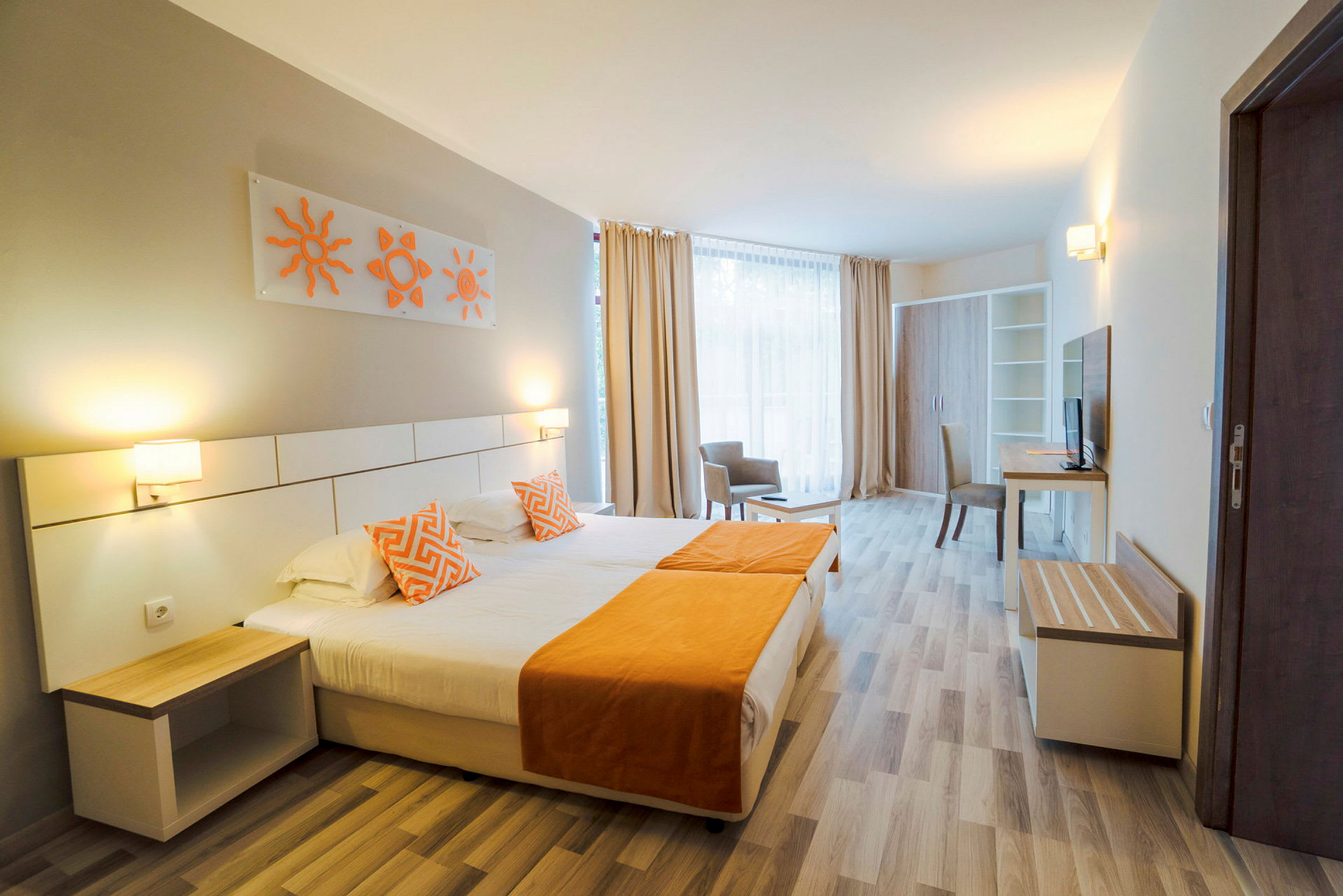 Et hotelværelse med en dobbeltseng med orange detaljer, to sengelamper og moderne indretning. Et stort vindue med lyse gardiner ses i baggrunden. (AI-genereret tekst)