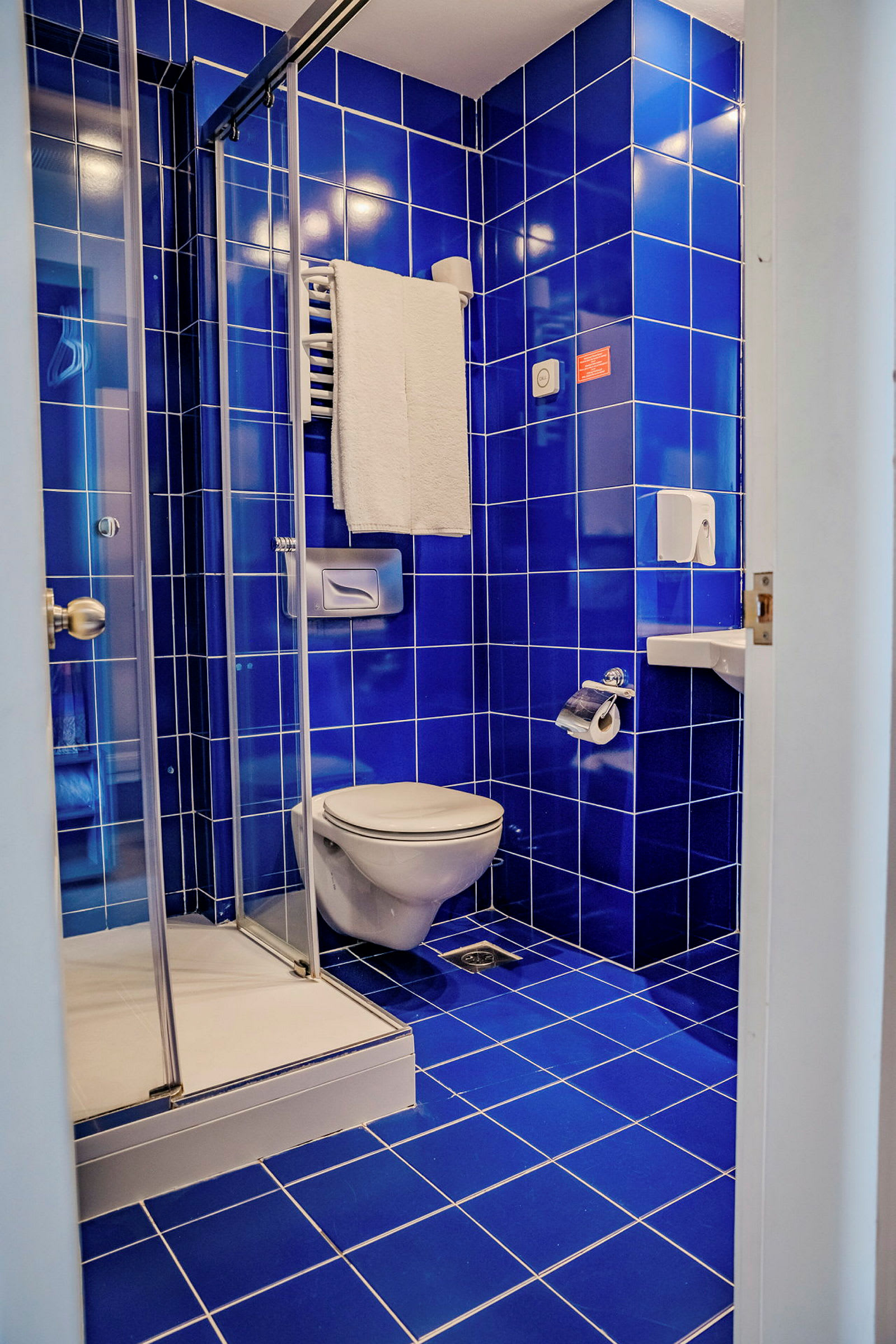 Et badeværelse med blå flisevægge og blå flisegulv, toilet, håndvask og brusebad. (AI-genereret tekst)