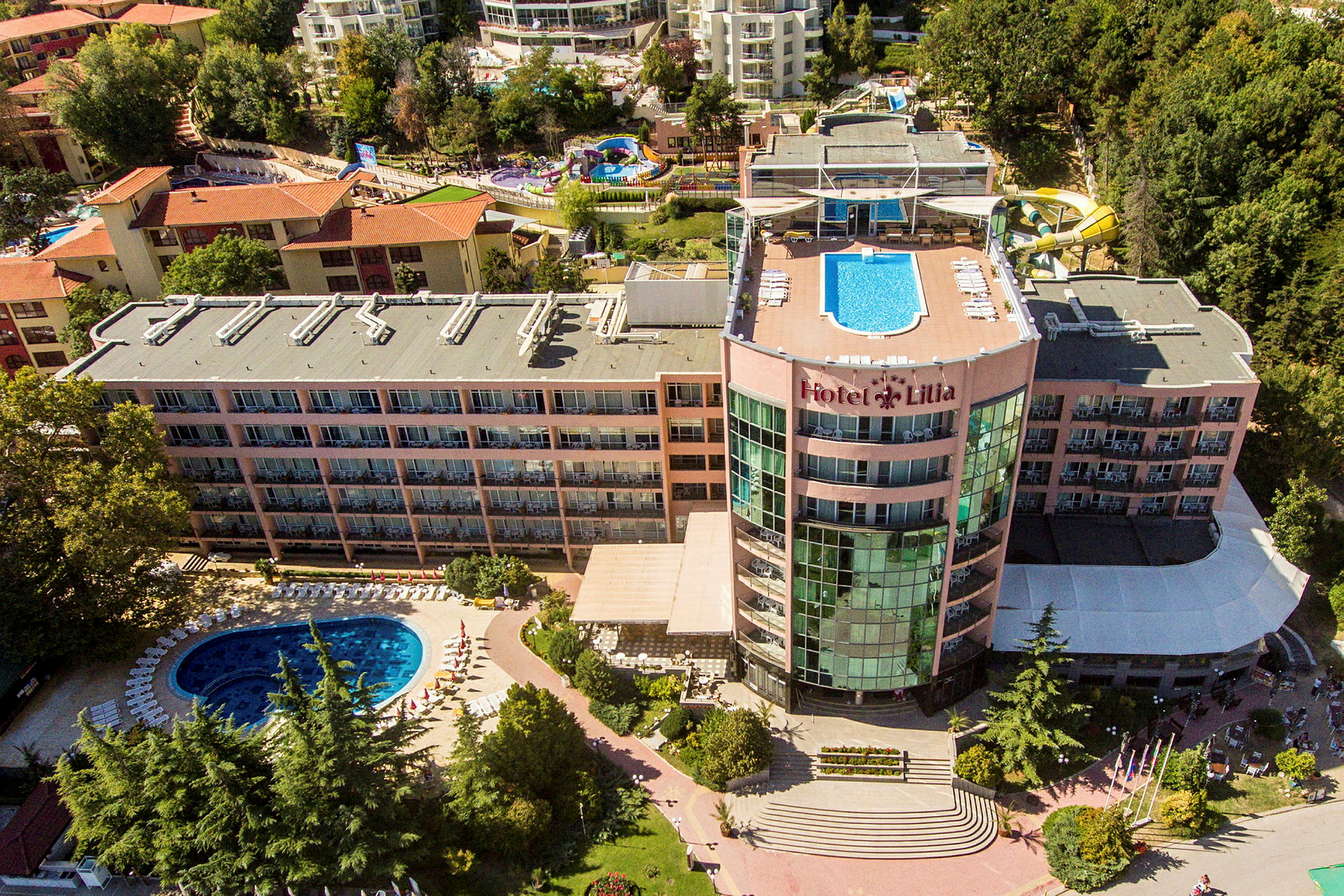 En hotelbygning med en pool på taget og en pool på jordplan, omgivet af grønne områder. (AI-genereret tekst)