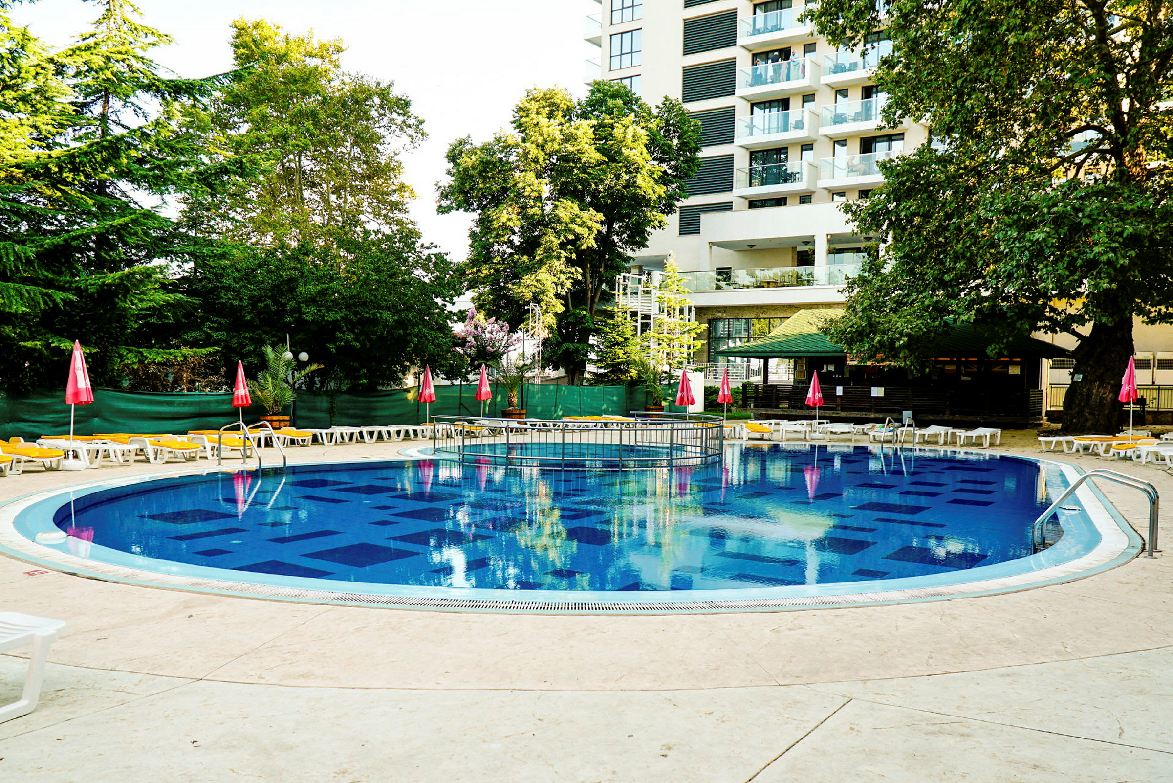 Udendørs swimmingpool med liggestole og parasoller ved kanten. (AI-genereret tekst)