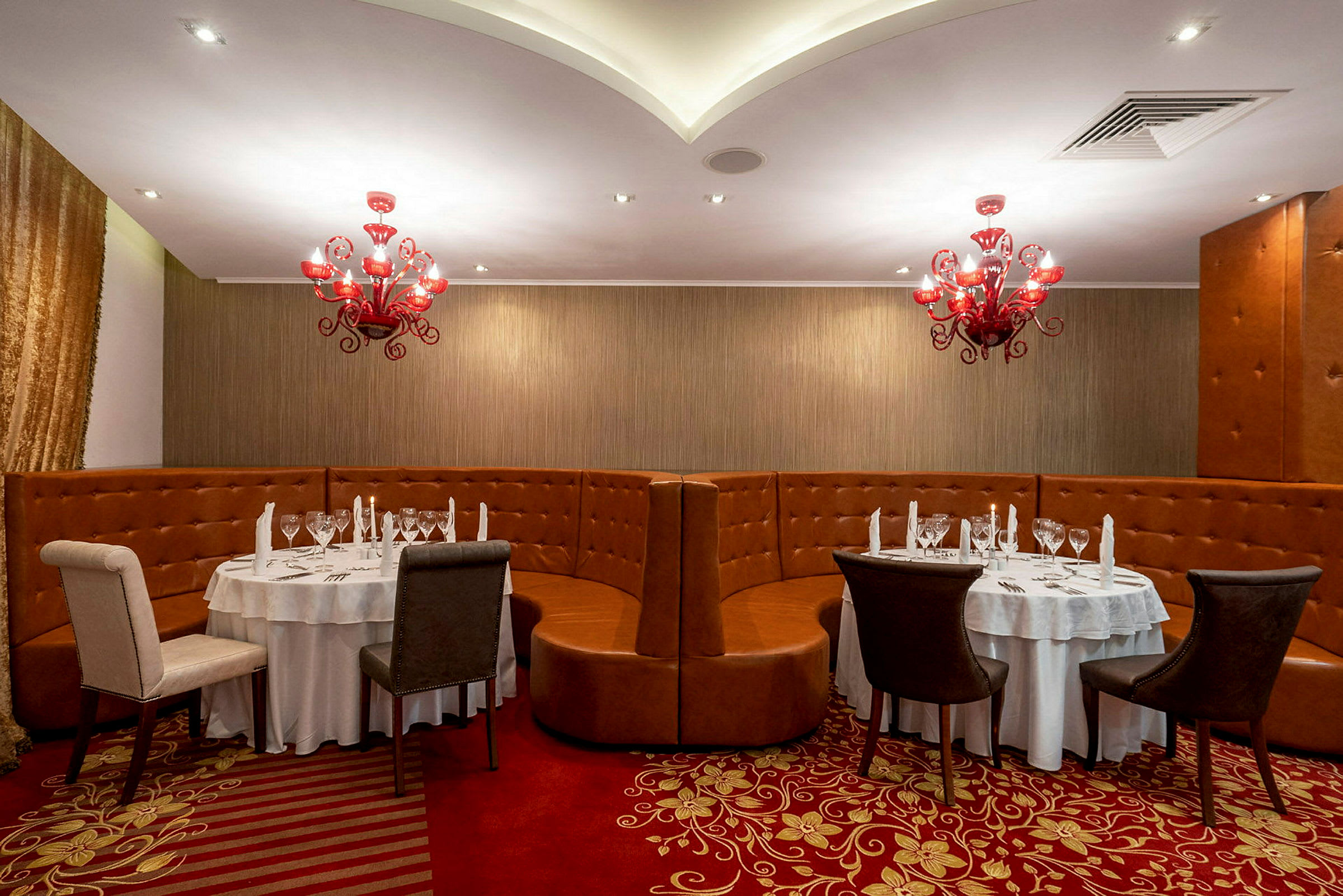 En restaurant med runde borde, stole og røde lysekroner. (AI-genereret tekst)