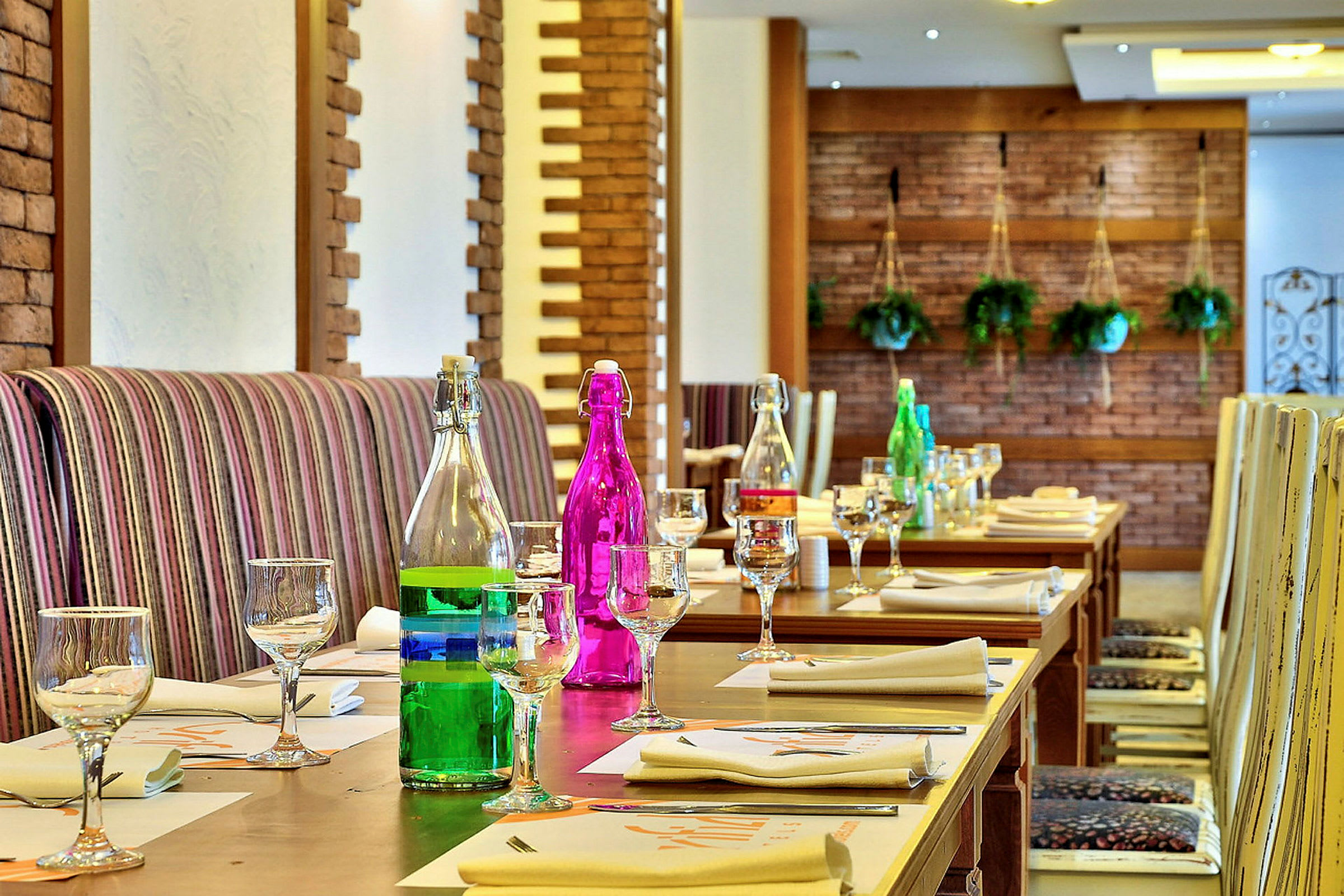Et indendørsbord dækket med glas og farverige flasker i en restaurant med vægdekorationer. (AI-genereret tekst)
