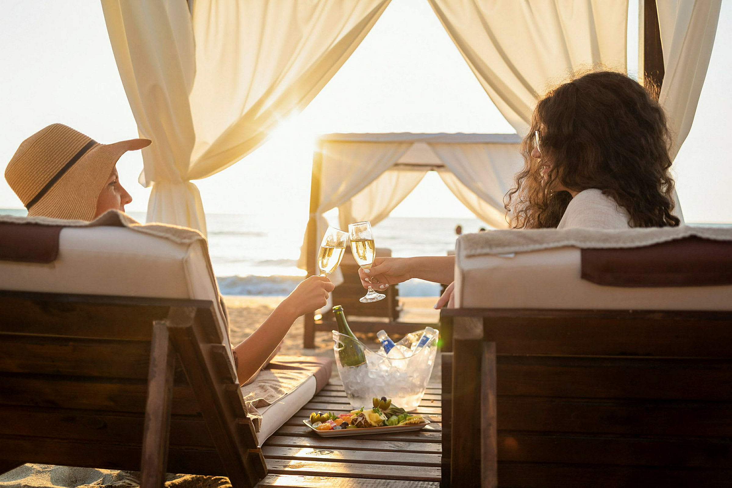 To personer skåler med glas på en strand under en baldakin. (AI-genereret tekst)