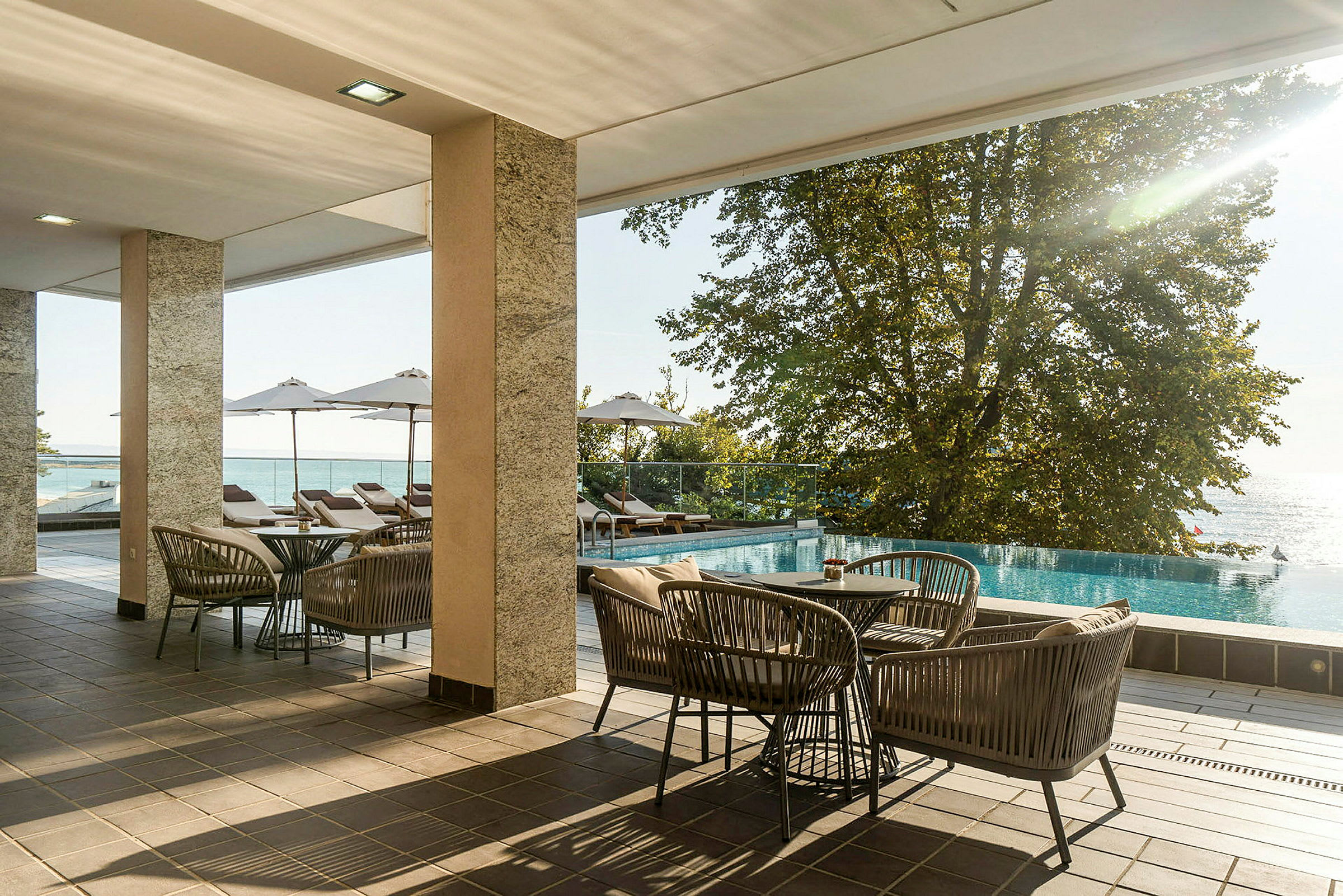 Møbleret terrasse med udsigt over en pool og havet. (AI-genereret tekst)