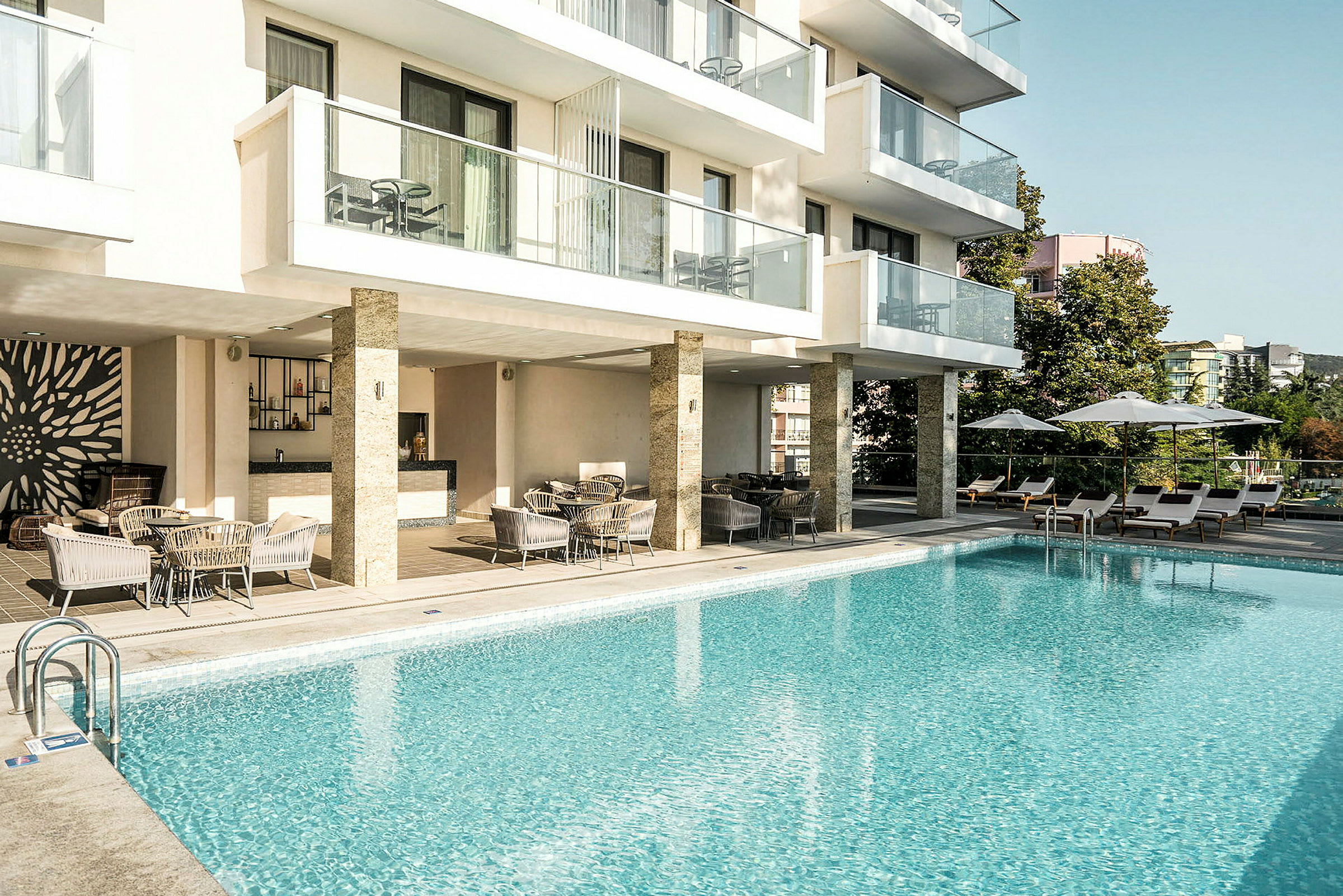 Eksteriør af et hotel med en udendørs pool, liggestole og siddeområde. (AI-genereret tekst)