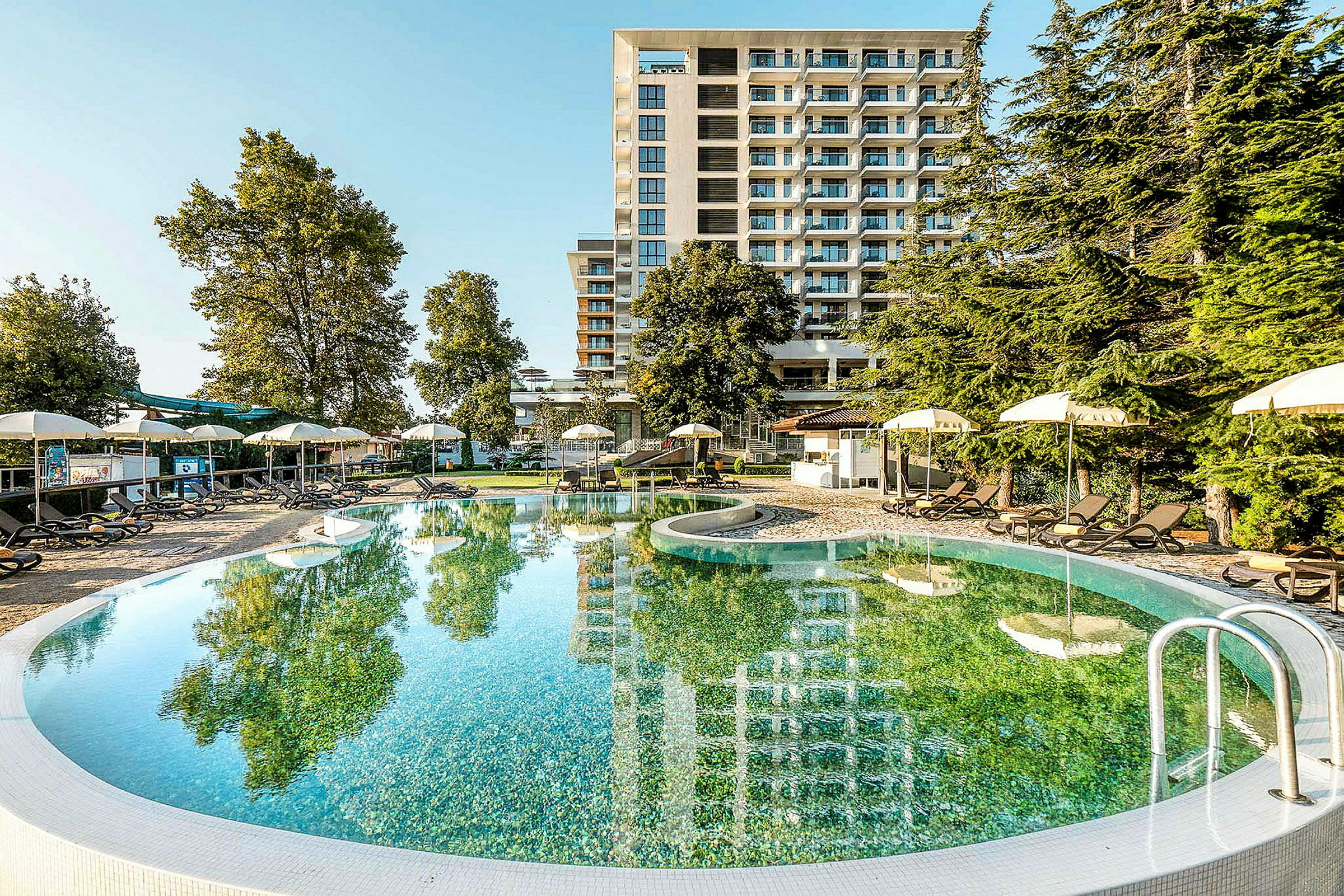 Opvarmet udendørs pool med liggestole og parasoller foran et moderne hotel. (AI-genereret tekst)