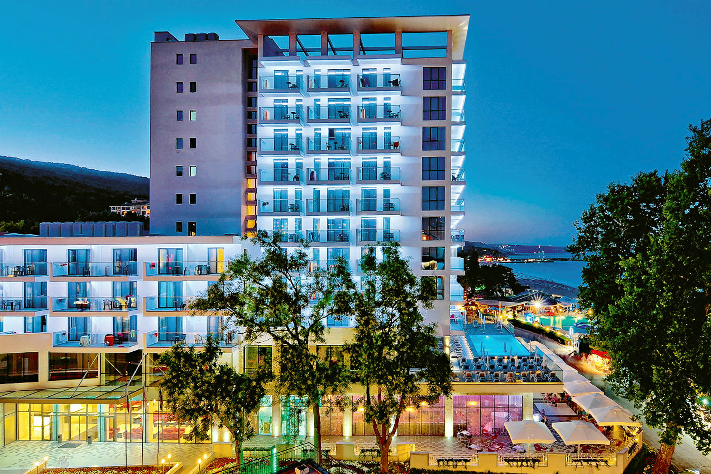 Moderne hotelbygning oplyst om aftenen, med pool og omgivelser. (AI-genereret tekst)
