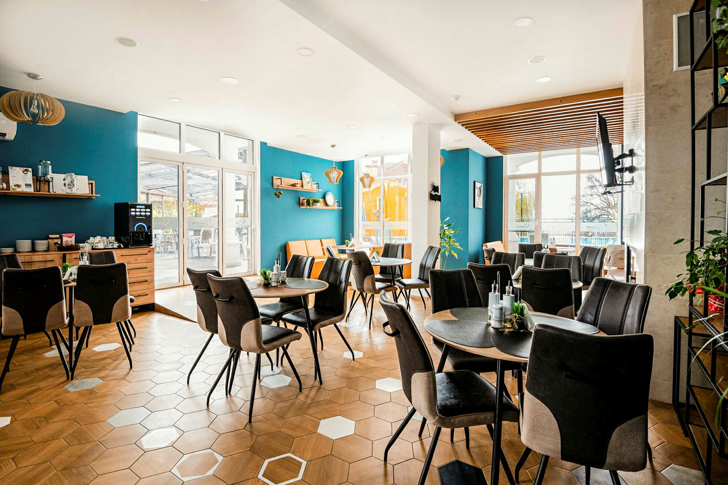 En lys og moderne indrettet café med blå vægge, sekskantet trægulv og flere borde med komfortable stole. (AI-genereret tekst)