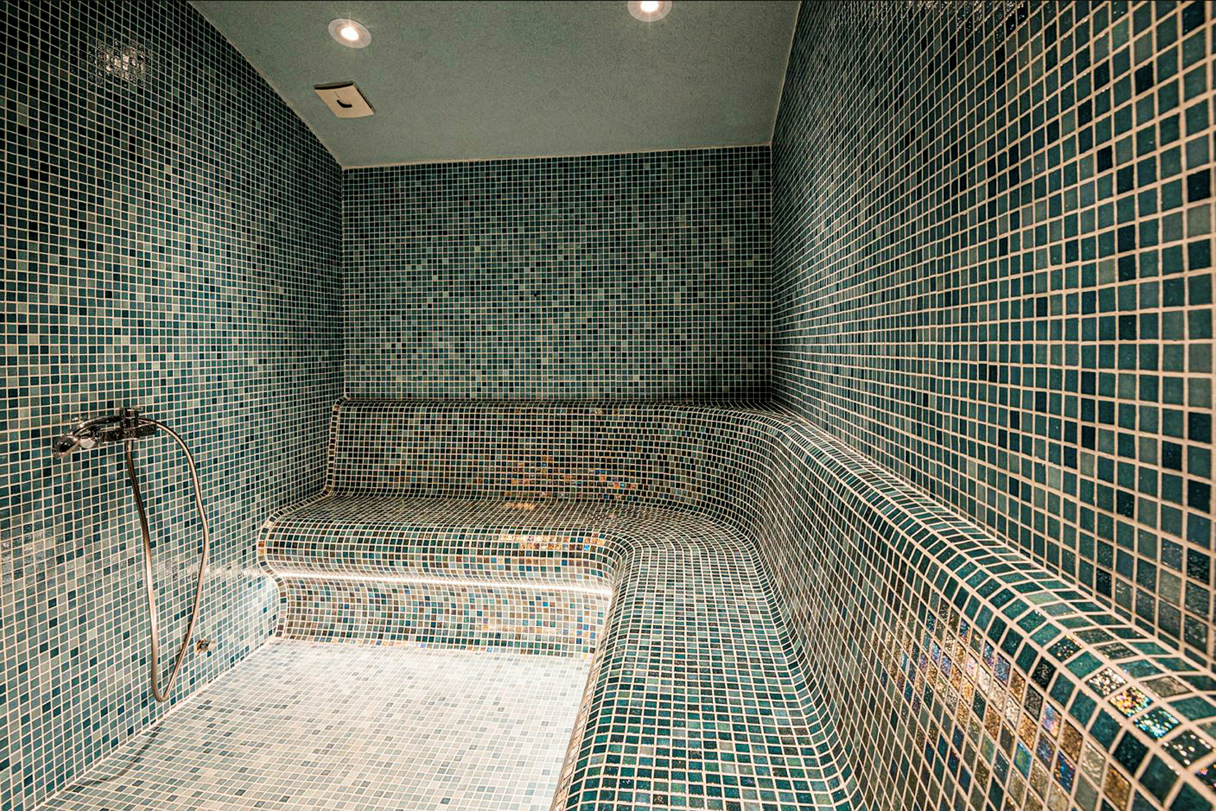 Et dampbad med vægge, gulv og siddebænke dækket af grønne mosaikfliser. (AI-genereret tekst)
