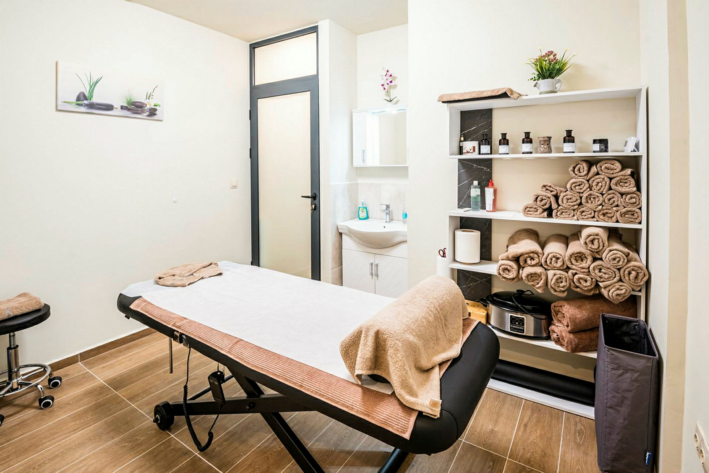 Et massage- eller behandlingsrum med briks, håndklæder på hylder og håndvask. (AI-genereret tekst)