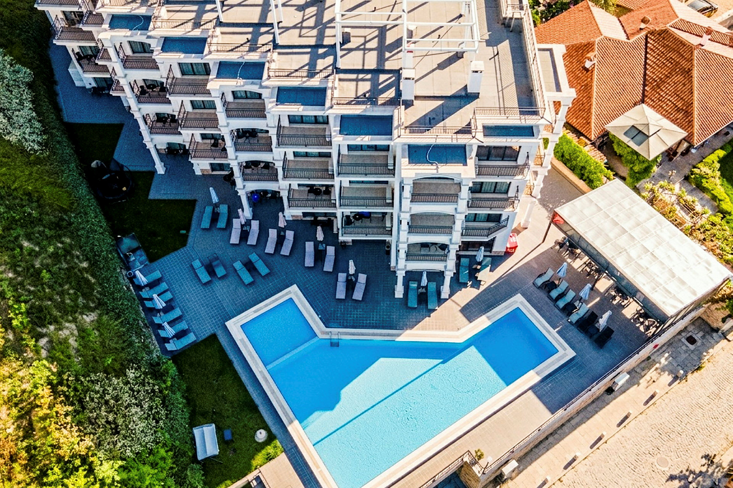 Luftfoto af en hotelbygning med en pool og liggestole udenfor. (AI-genereret tekst)