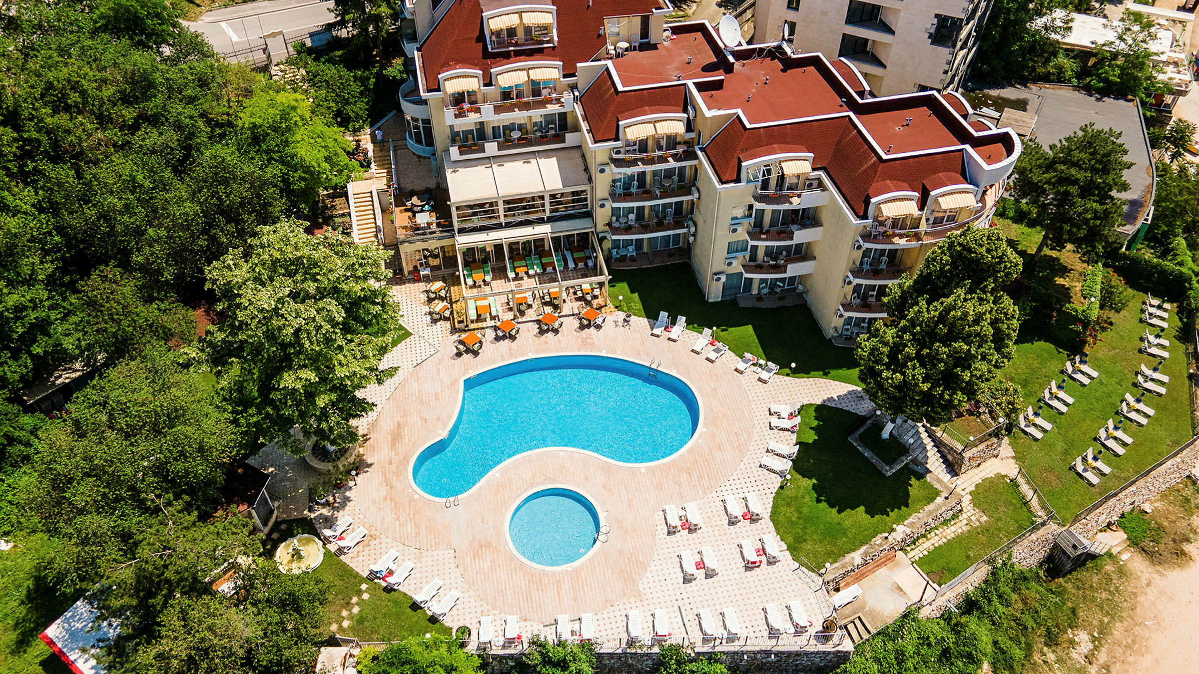 Luftfoto af hotelkompleks med pool og omkringliggende grønt. (AI-genereret tekst)