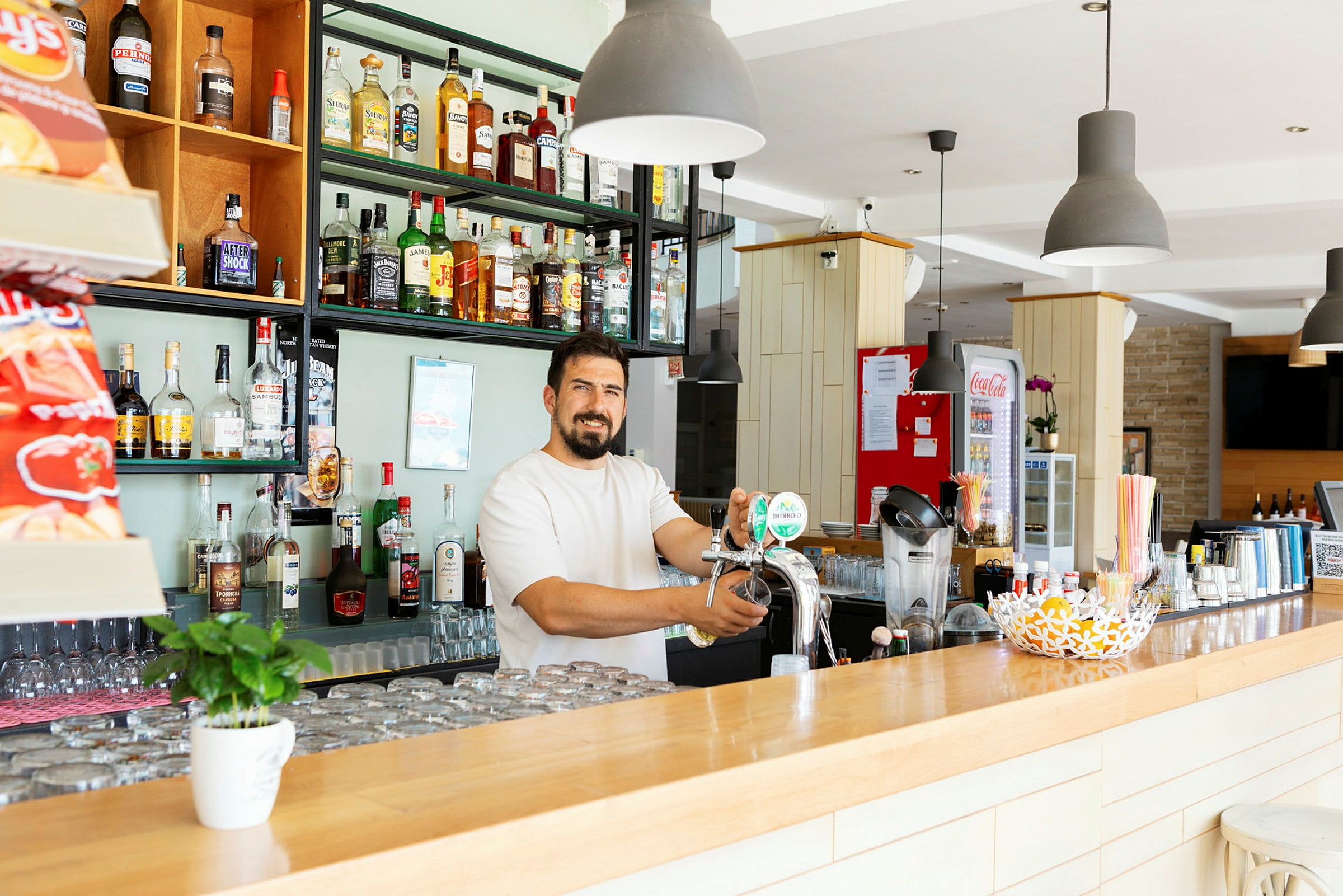 En bar med hylder fyldt med flasker og en person, der hælder øl fra en dispenser. (AI-genereret tekst)