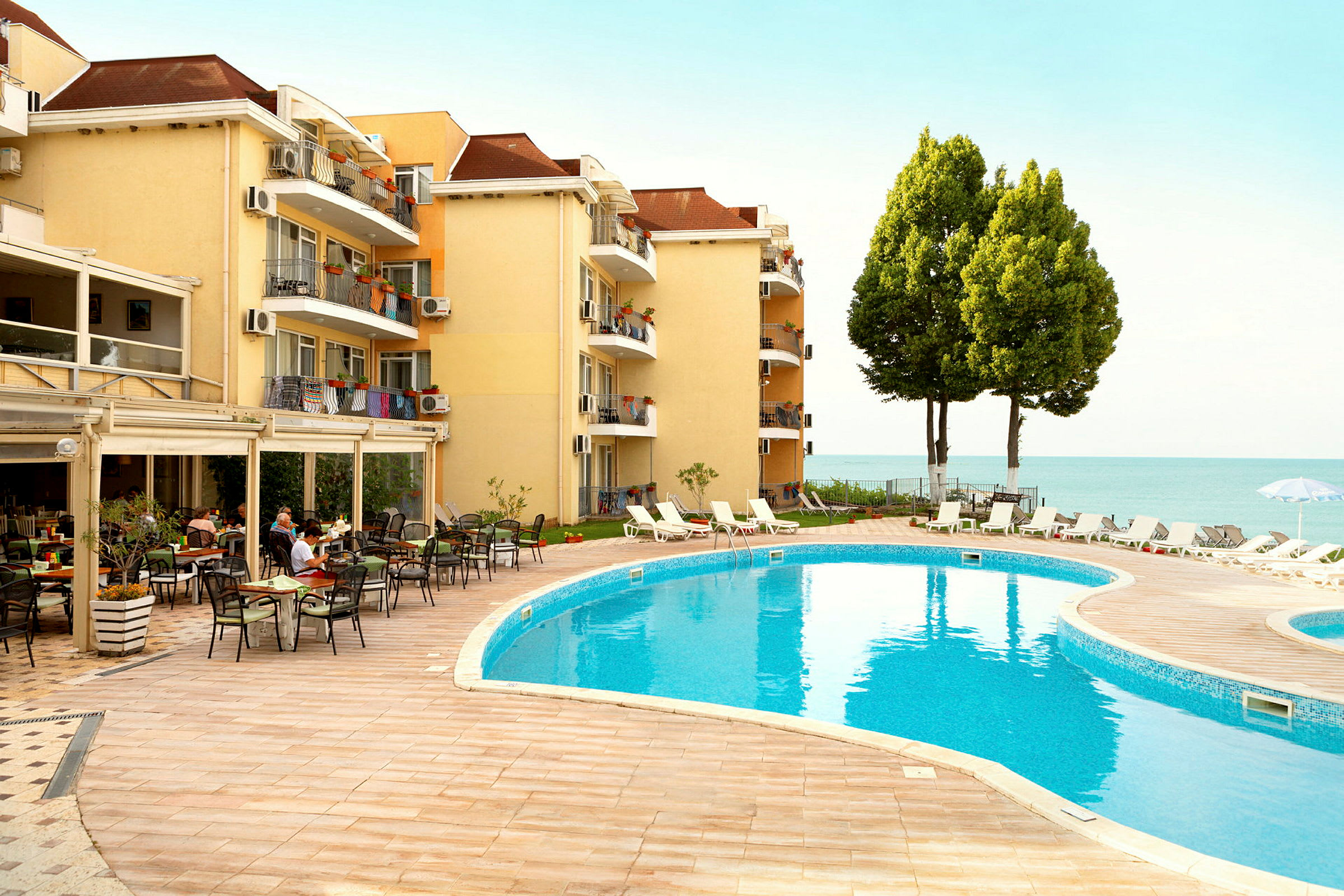 Hotelbygning ved en pool med liggestole og udsigt over havet. (AI-genereret tekst)
