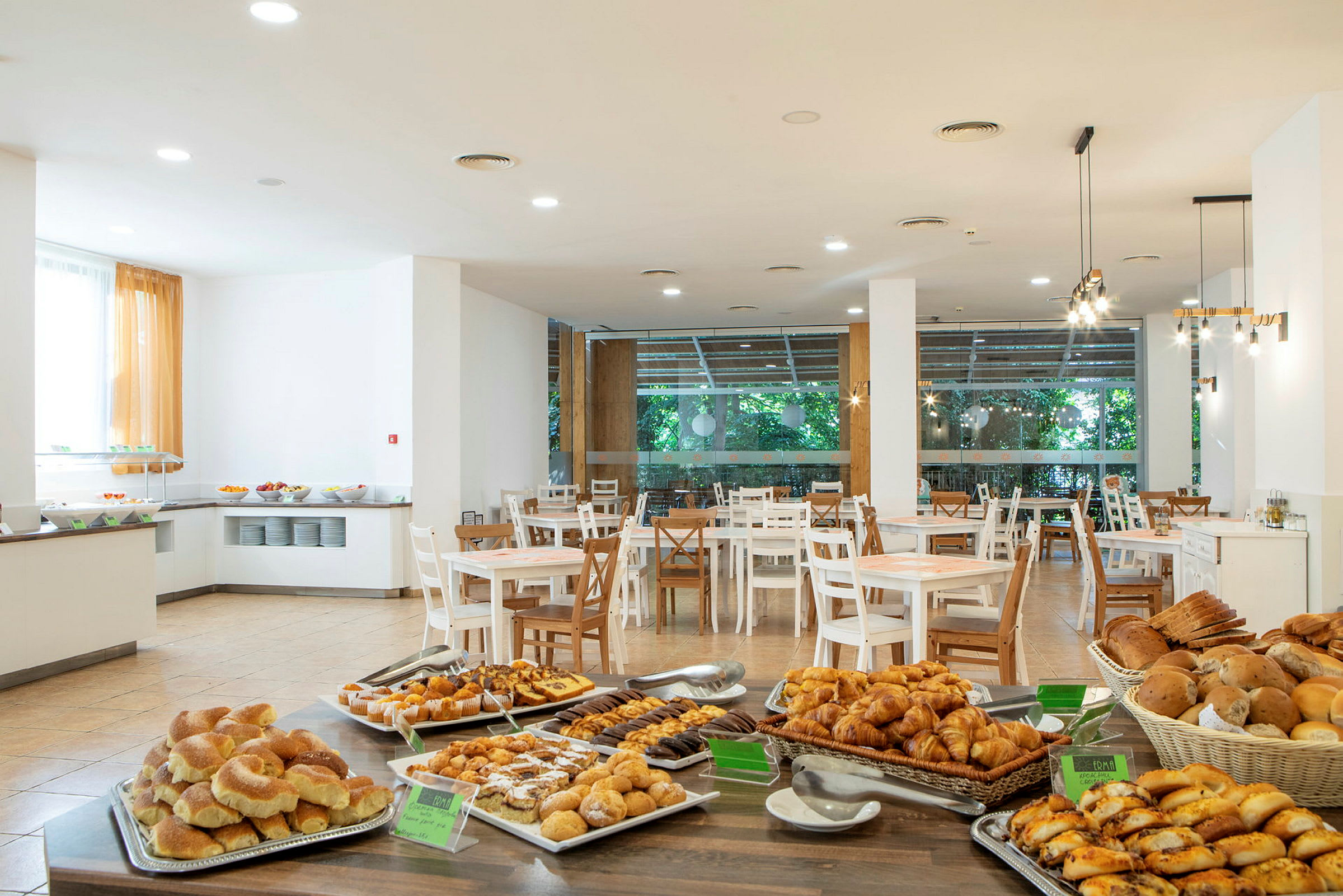 Et hotelrestaurantområde med borde og en buffet fyldt med forskellige brød og bagværk. (AI-genereret tekst)