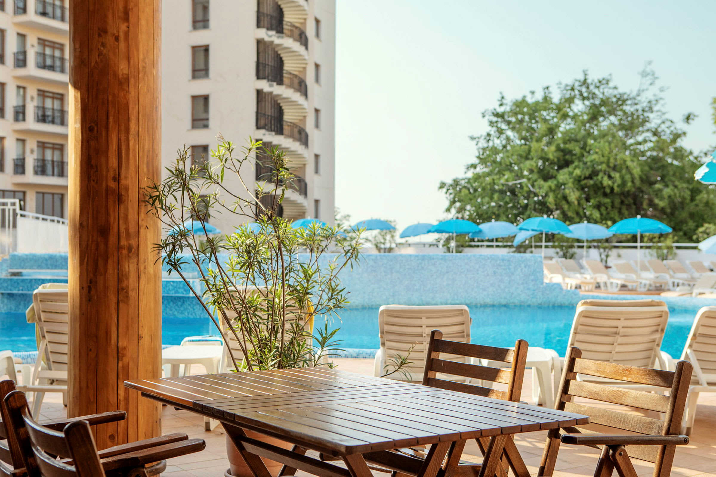 Billede af et hotelområde med en pool, solsenge og parasoller. (AI-genereret tekst)