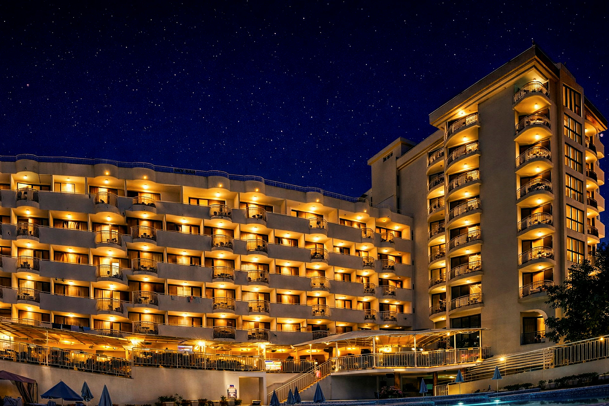 Hotelbygning med oplyste altaner og vinduer om aftenen under en stjerneklar nattehimmel. (AI-genereret tekst)