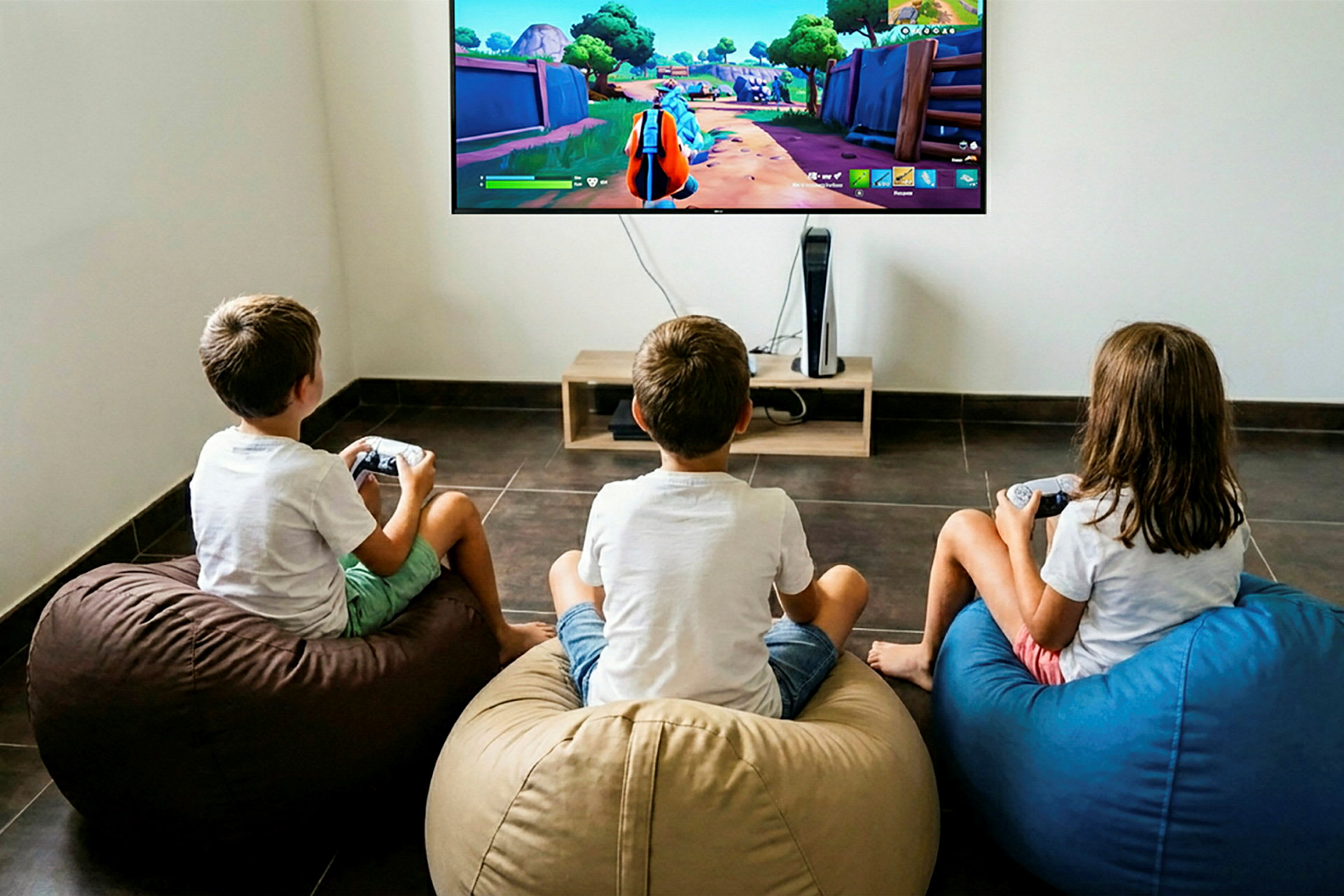 Tre børn sidder på sækkestole og spiller et videospil på en stor TV, der er monteret på væggen. (AI-genereret tekst)