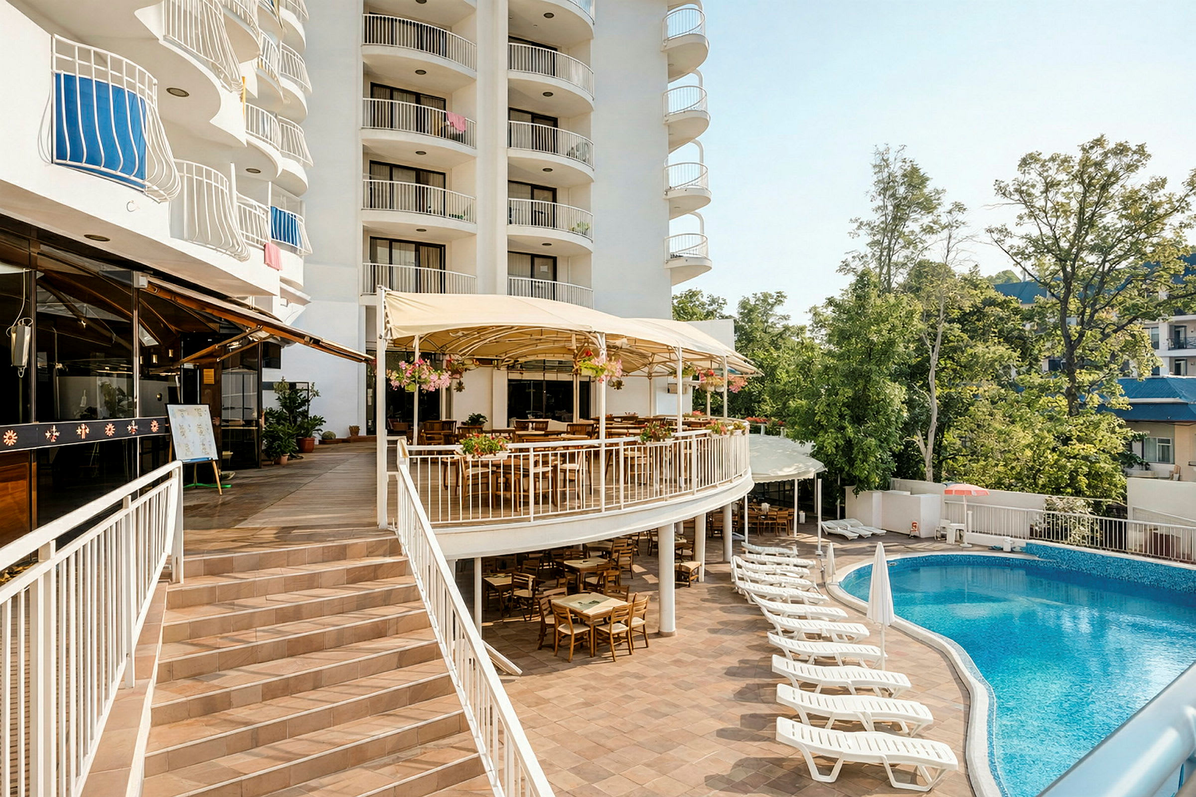 Et hotel med altaner, en hævet terrasse med udendørsservering og en pool med liggestole i forgrunden. (AI-genereret tekst)