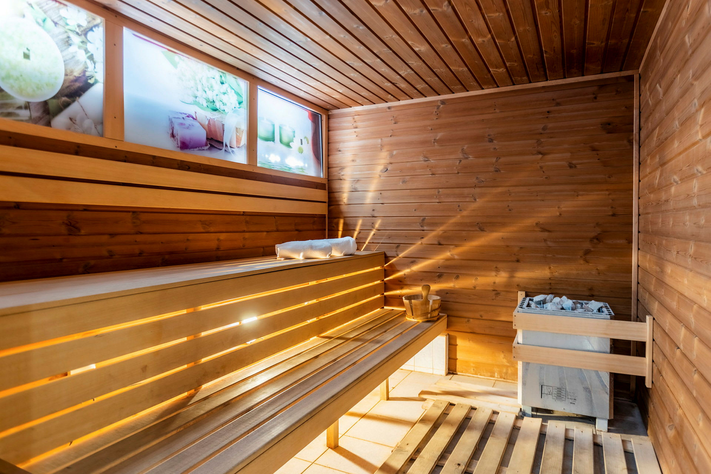 Et interiør af en sauna i træ med siddepladser og en varmekilde. (AI-genereret tekst)