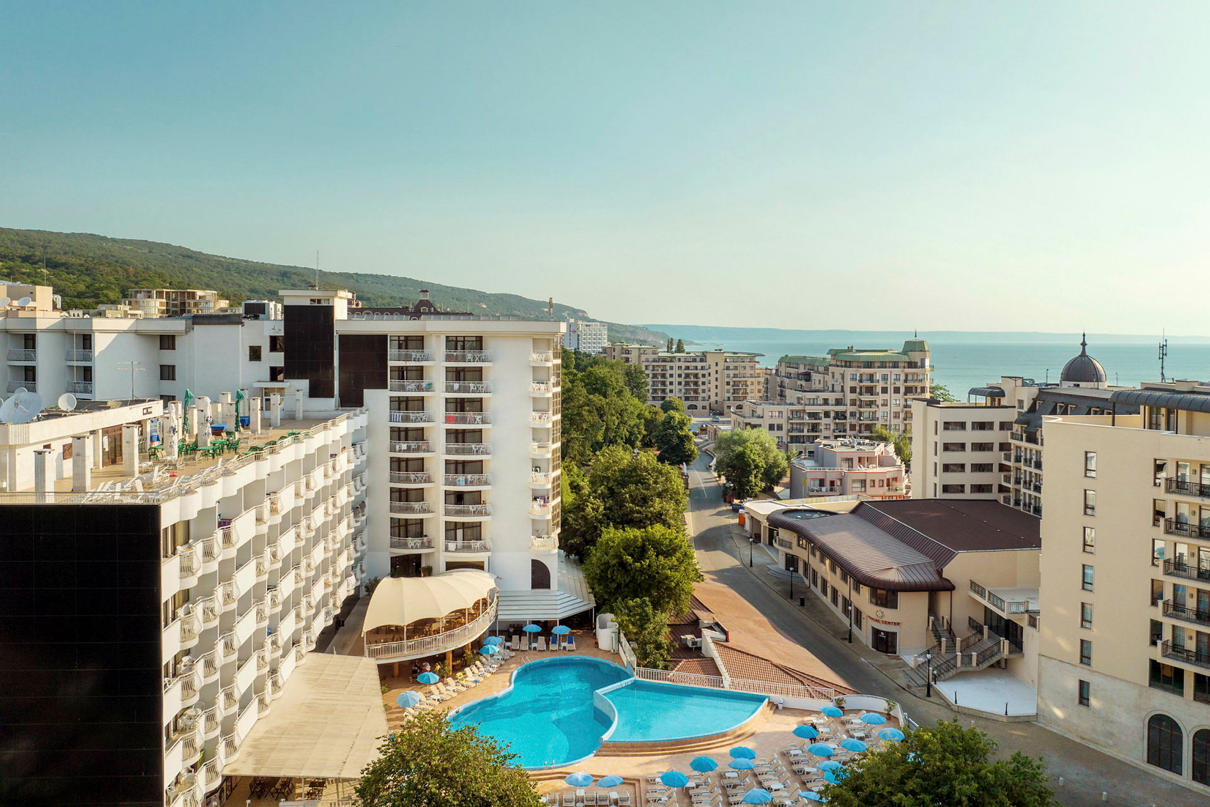 Hotelbygninger med en pool i forgrunden og havet i baggrunden. (AI-genereret tekst)