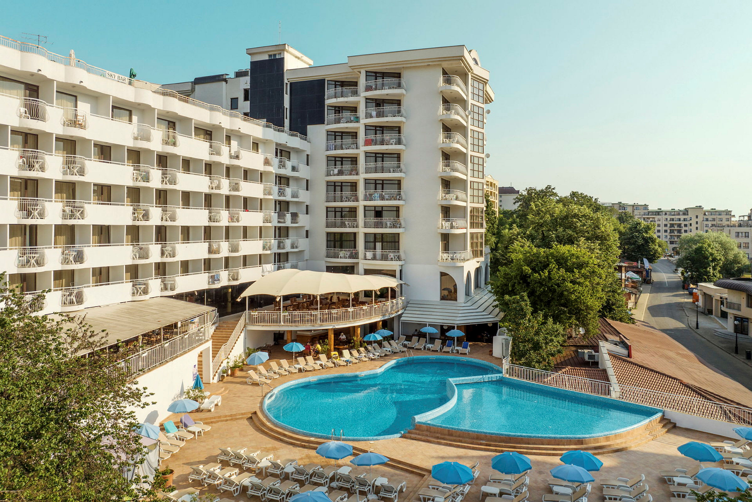 Hotelkompleks med en stor pool og liggestole omgivet af bygninger. (AI-genereret tekst)