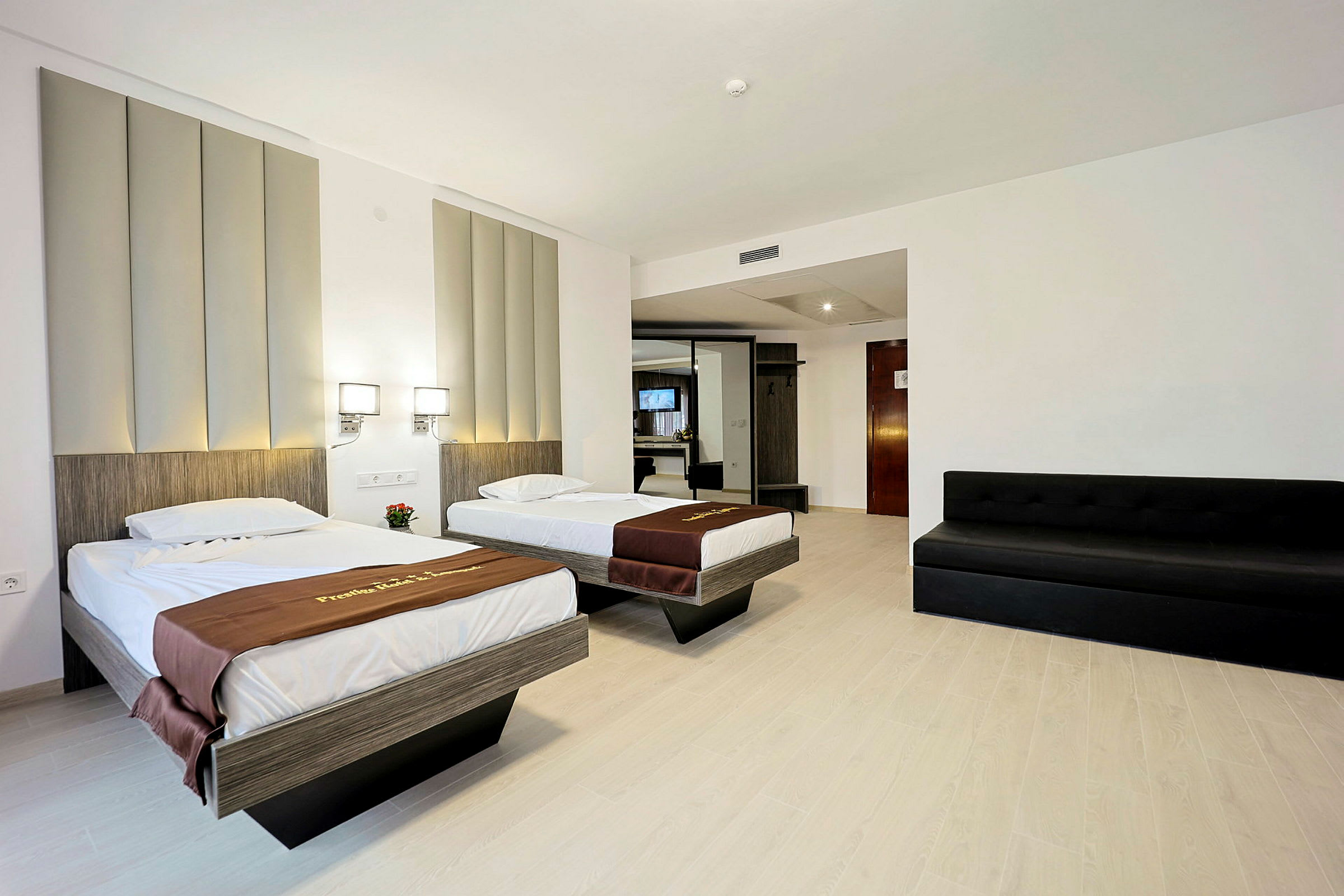 Hotelværelse med to enkeltsenge, en sort sofa og moderne indretning med et garderobeskab og spejl. (AI-genereret tekst)