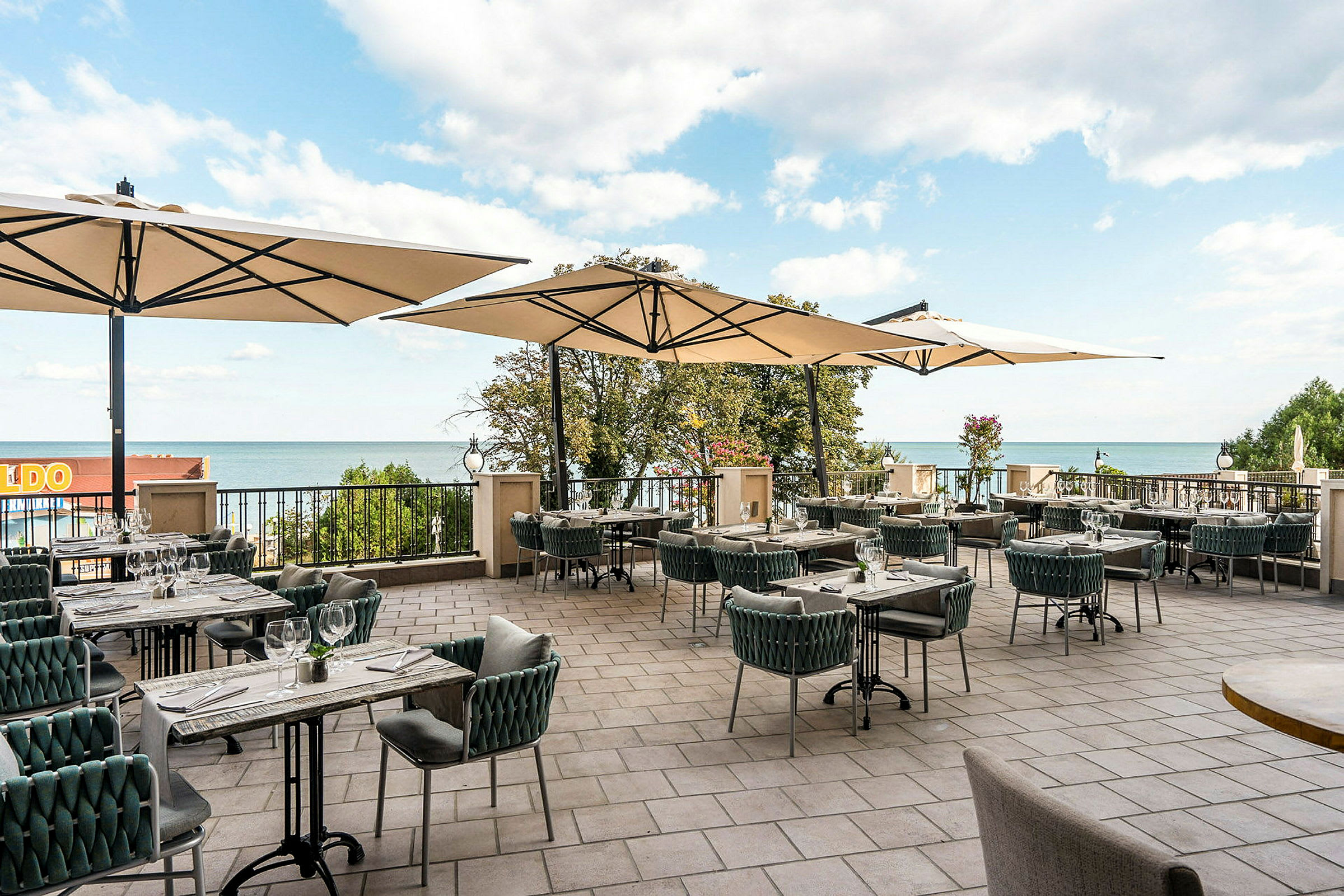 En terrasse med spiseborde, stole og parasoller, med udsigt til havet. (AI-genereret tekst)