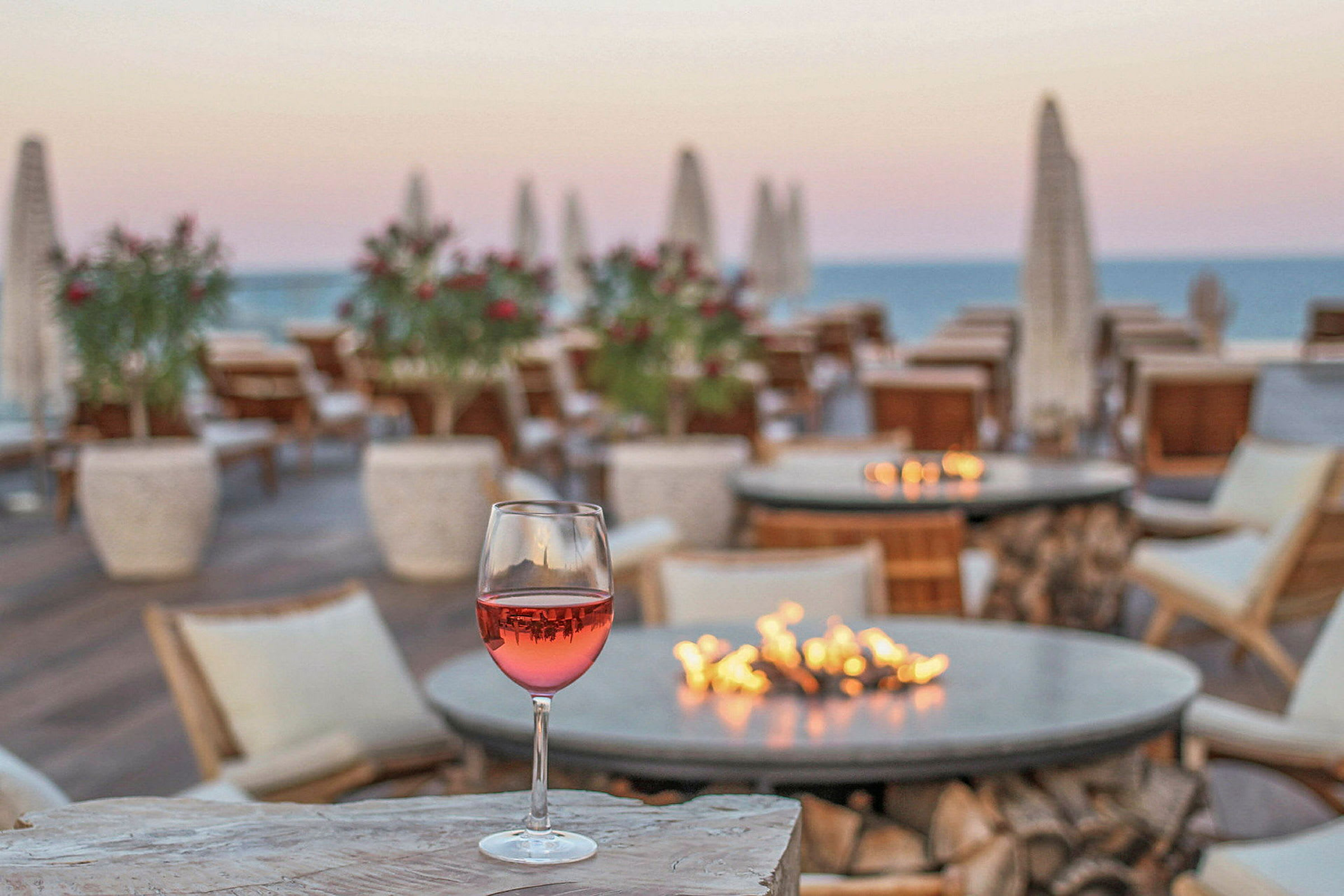 Et glas rosévin står på et stenbord i en udendørs restaurant med udsigt over havet og solnedgangen. (AI-genereret tekst)