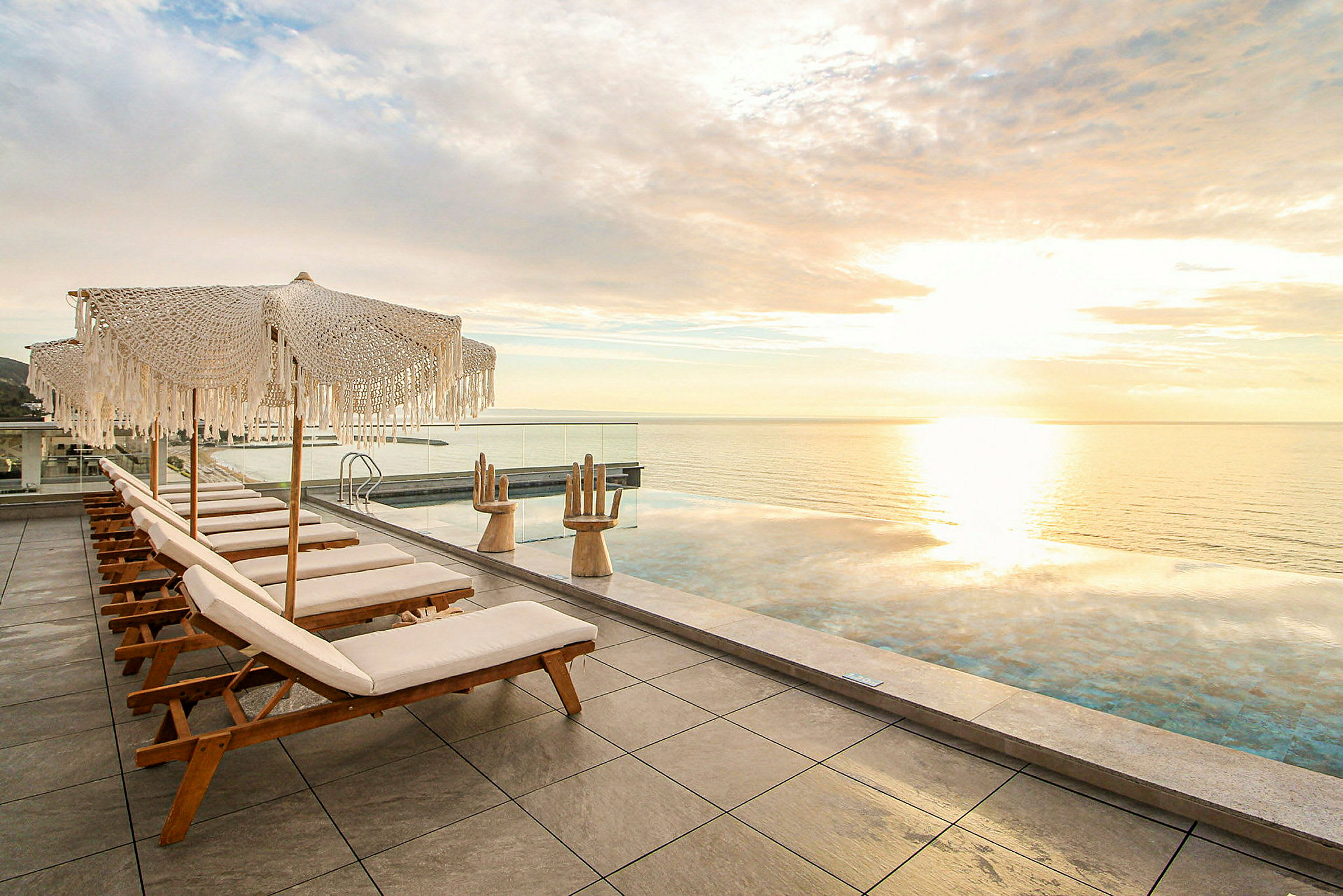 Liggestole og parasoller ved en infinitypool med udsigt over havet. (AI-genereret tekst)