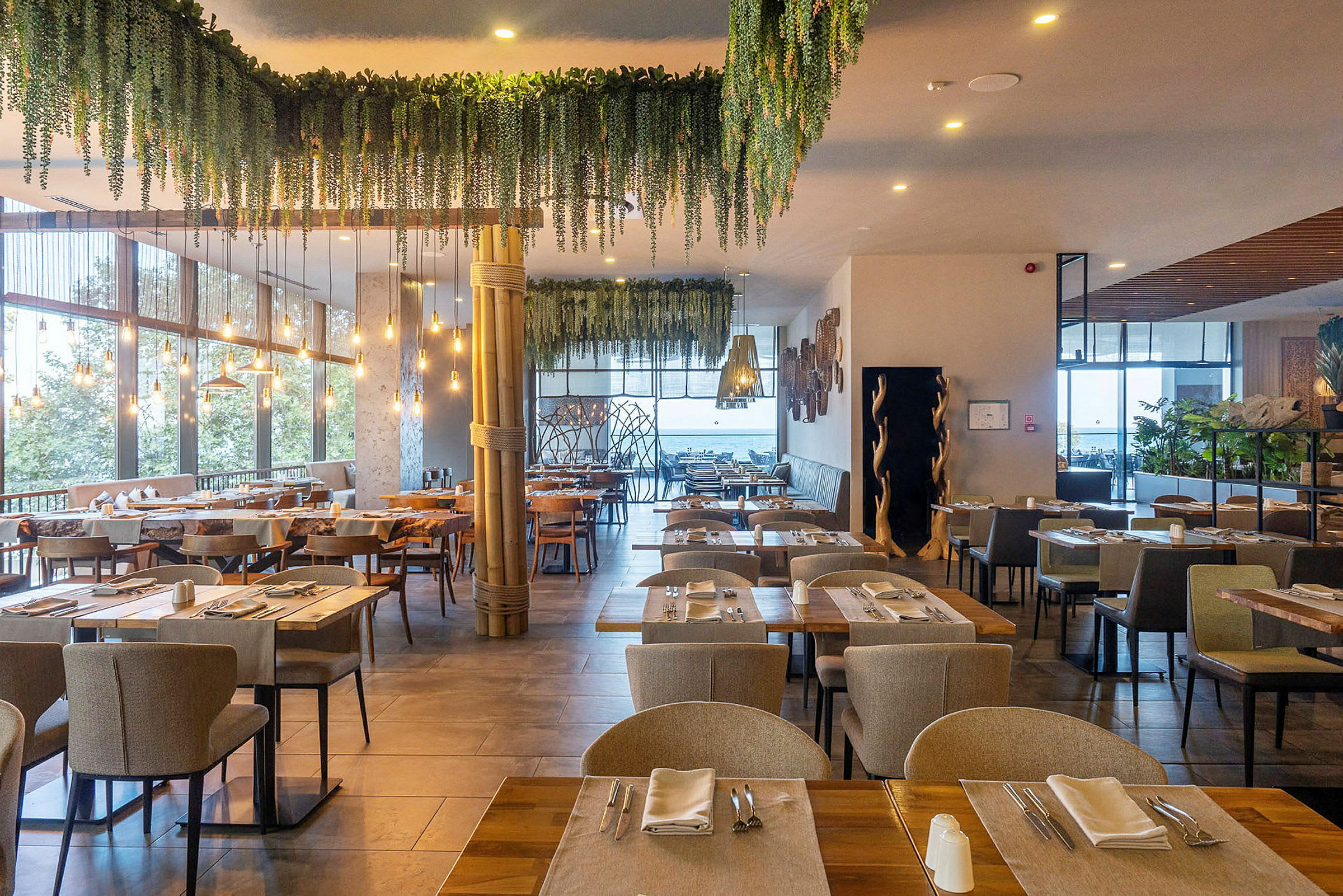 En restaurant med borde dækket til servering, omgivet af grøn dekoration og lyskilder. (AI-genereret tekst)