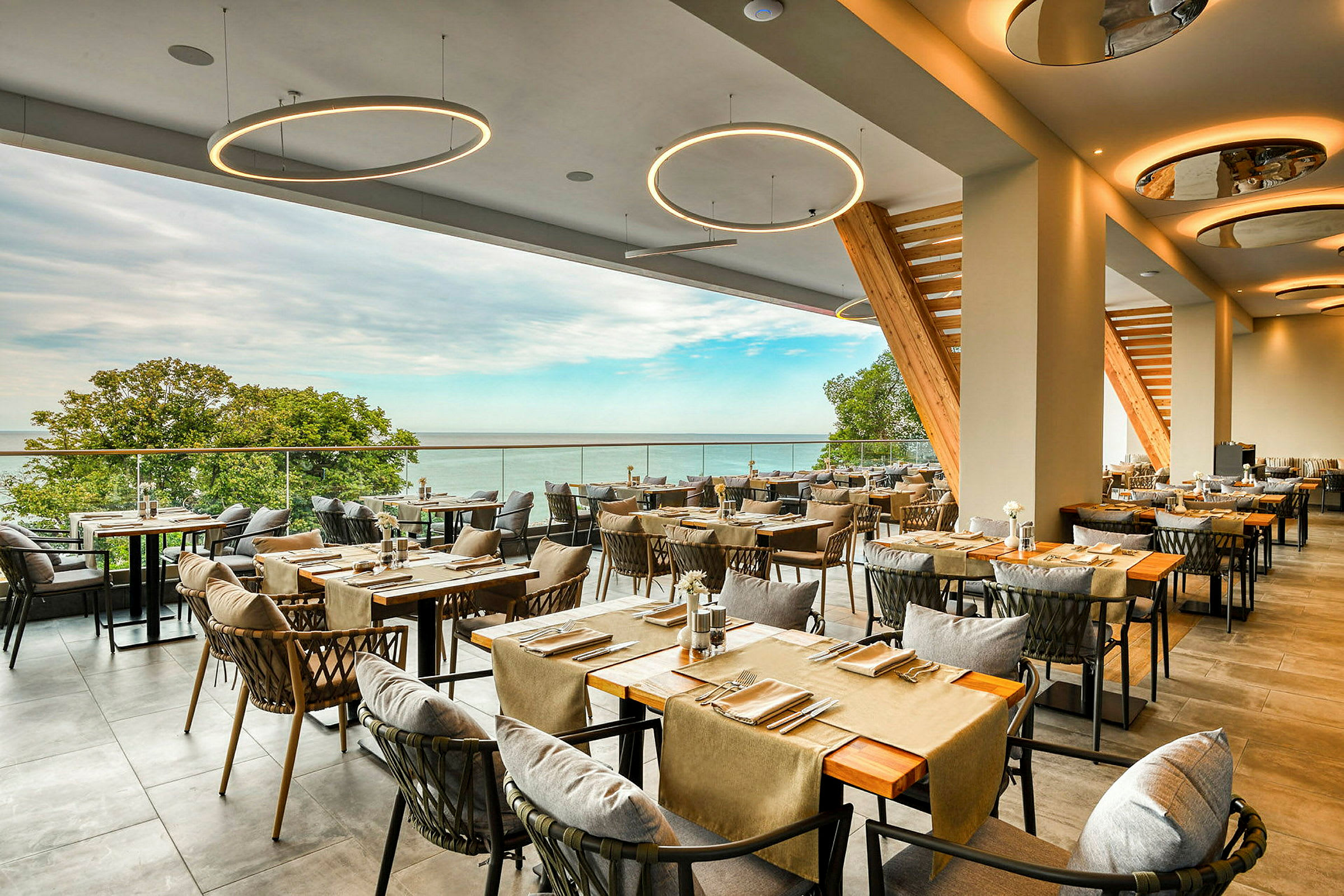 Restaurant med moderne indrettede borde og stole samt udsigt over havet og grøn natur. (AI-genereret tekst)