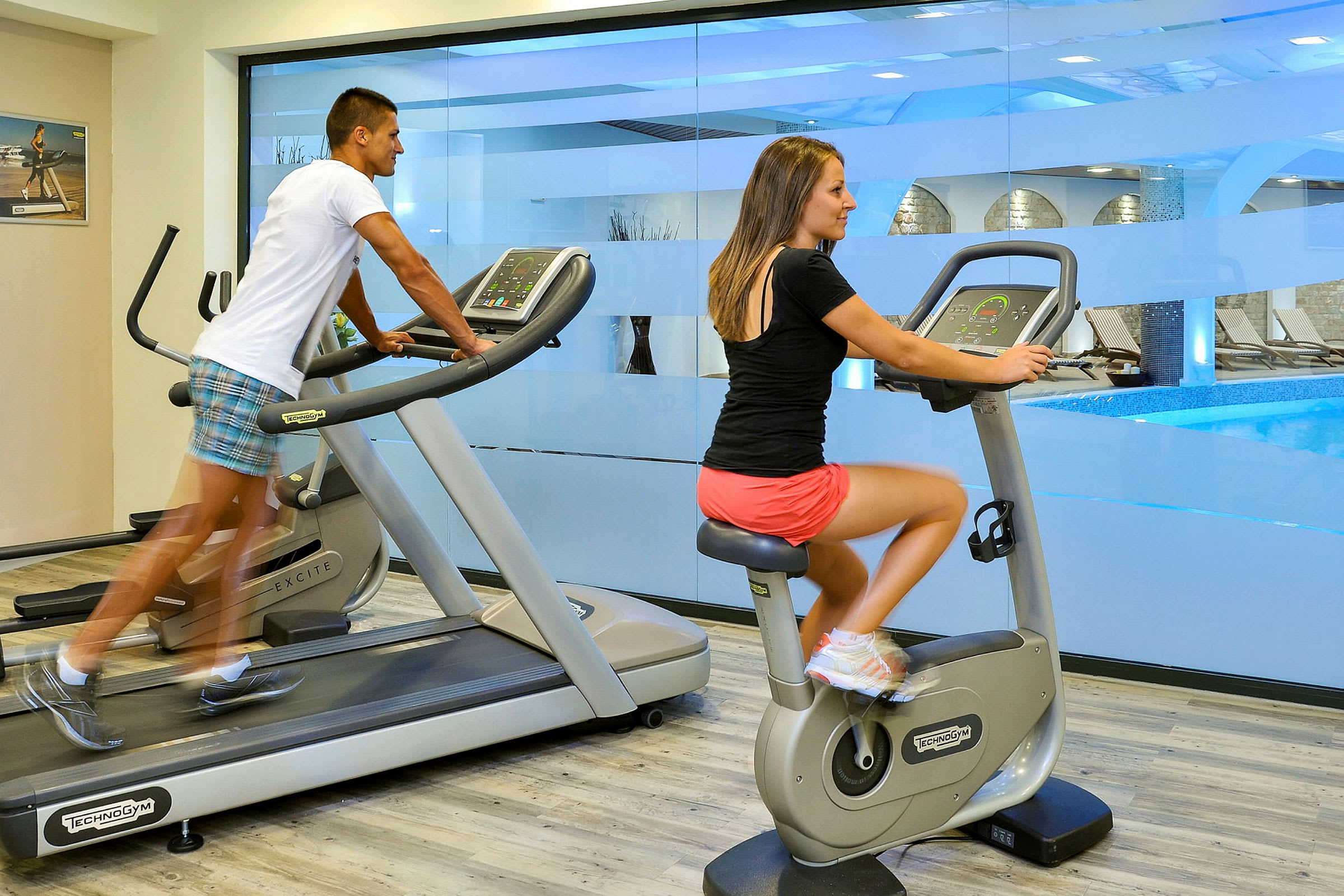 Træningscenter med fitnessudstyr og vindue mod en pool. (AI-genereret tekst)